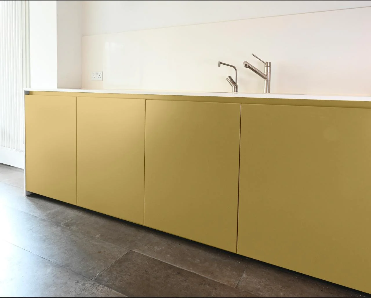 Modern kitchen cabinet with yellow doors, stainless steel faucet, white countertop, and a plain white wall in the background.