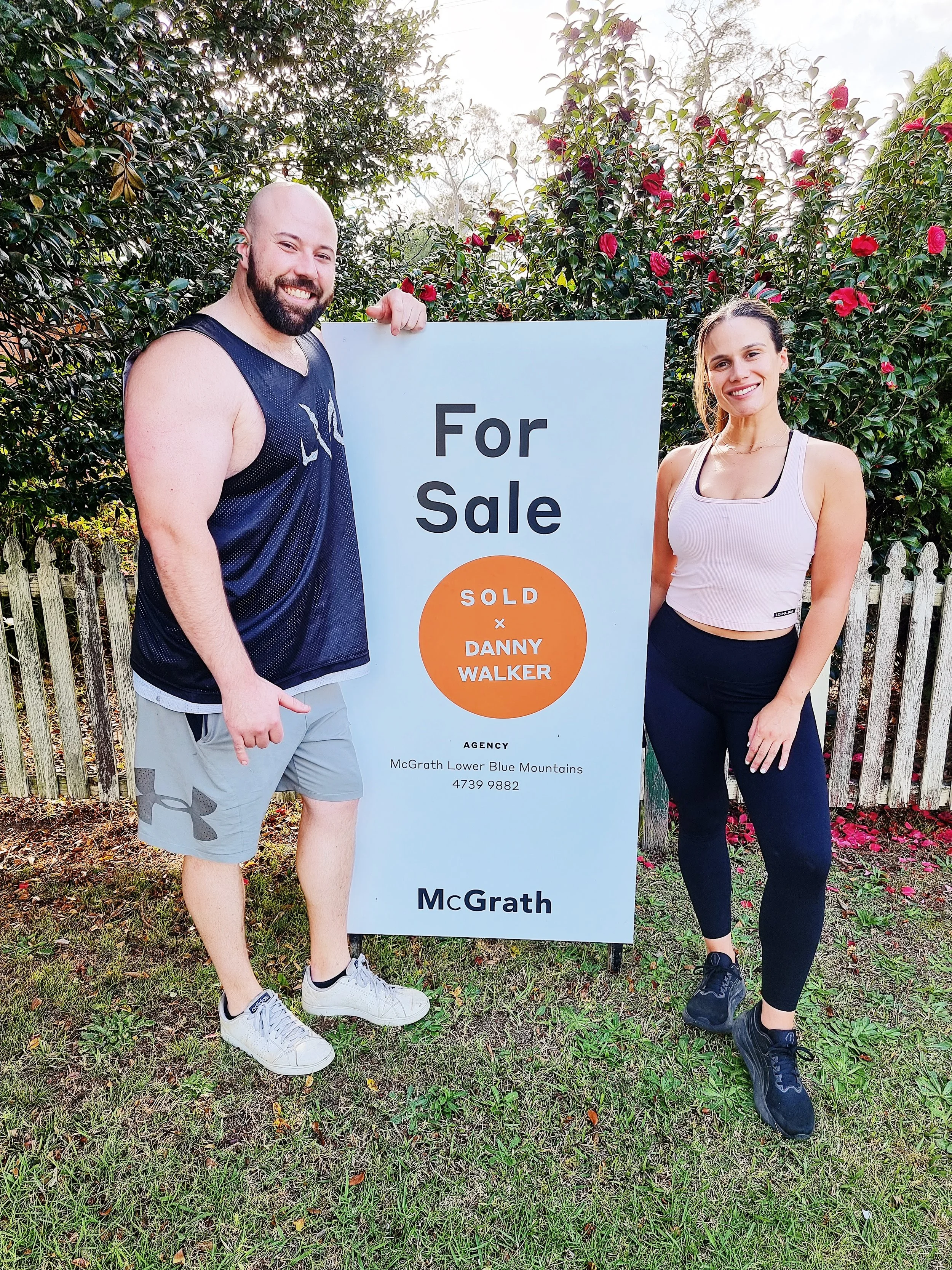 Happy buyers in Blaxland standing beside a sold sign for their new home — another successful result with Danny Walker Real Estate.