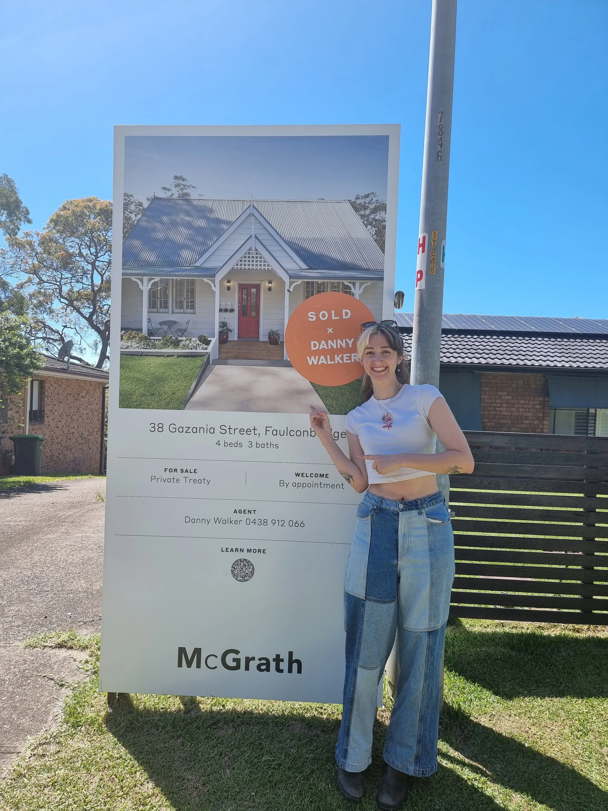 Happy buyer celebrating in front of a sold sign at 38 Gazania Street, Falconbridge — another outstanding Blue Mountains sale with Danny Walker Real Estate.