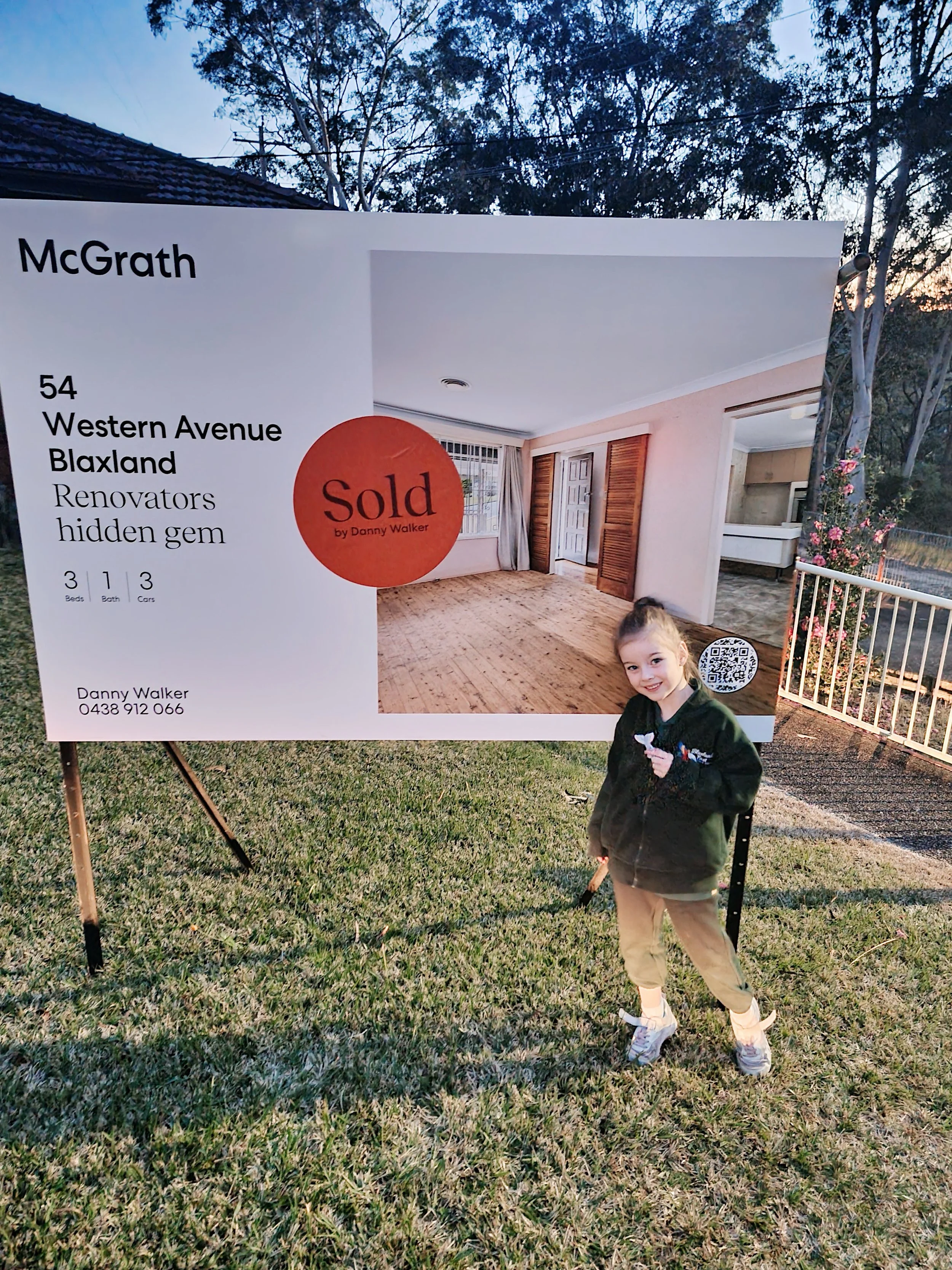 Young girl standing beside a sold real estate sign in Blaxland NSW, marking another successful family home sale with Danny Walker Real Estate.