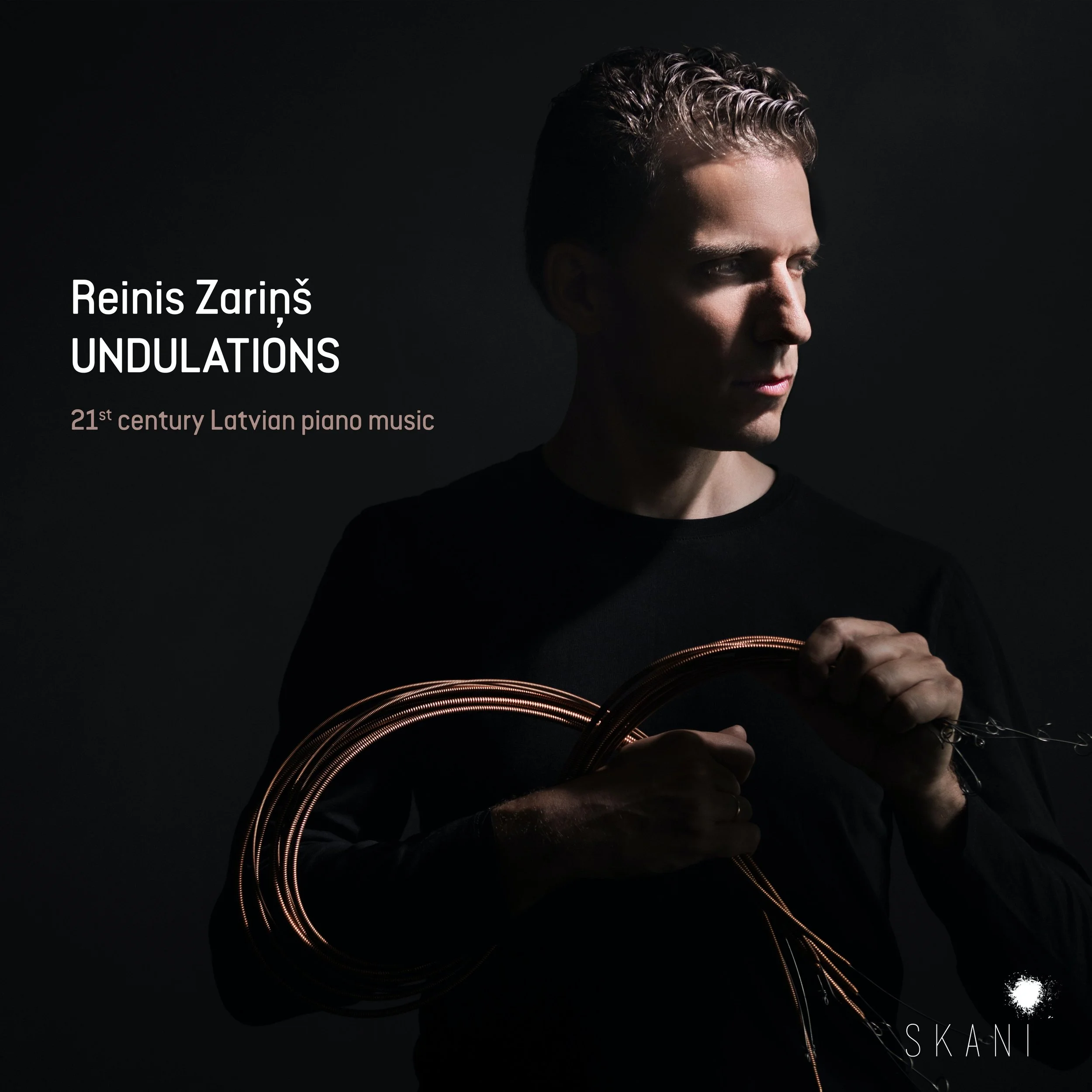 The front cover of Undulations album shows portrait of pianist Reinis Zariņš holding a set of copper strings from piano