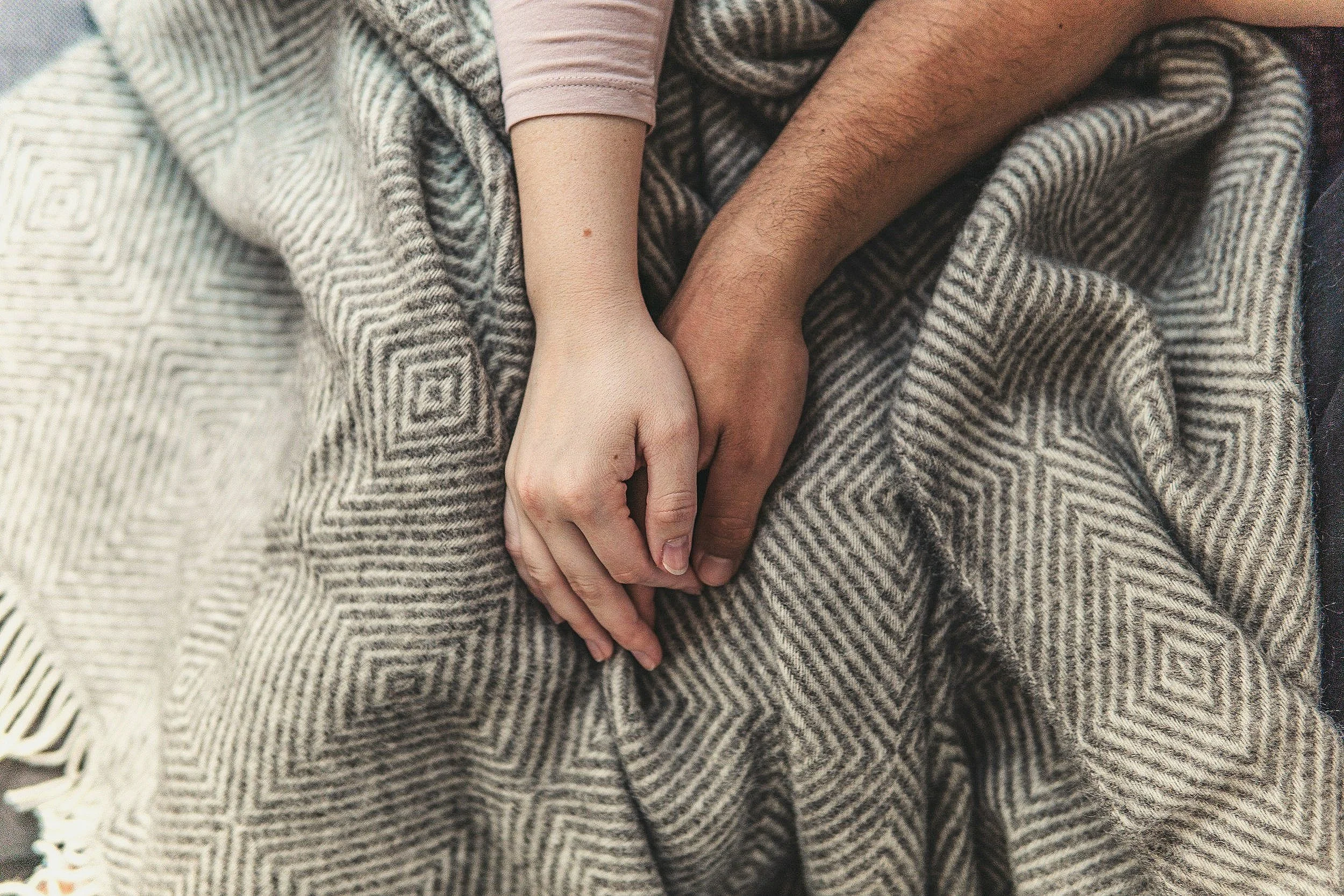 Two people holding hands on a patterned blanket.