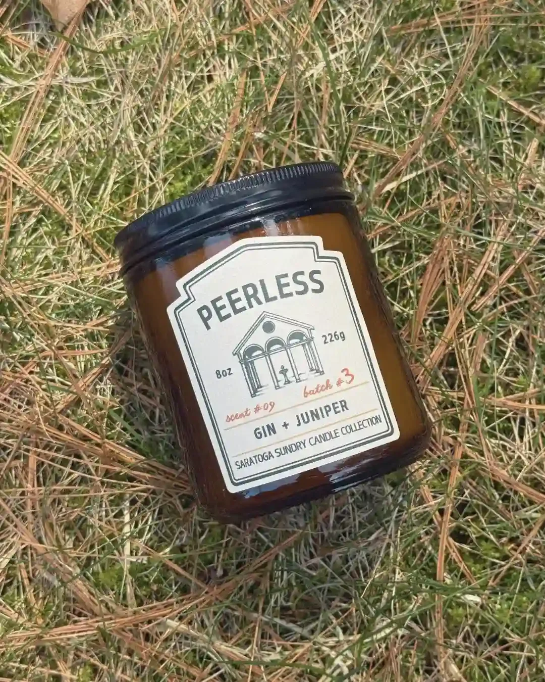 Peerless soy candle in amber jar from Saratoga Sundry laying in grass.webp