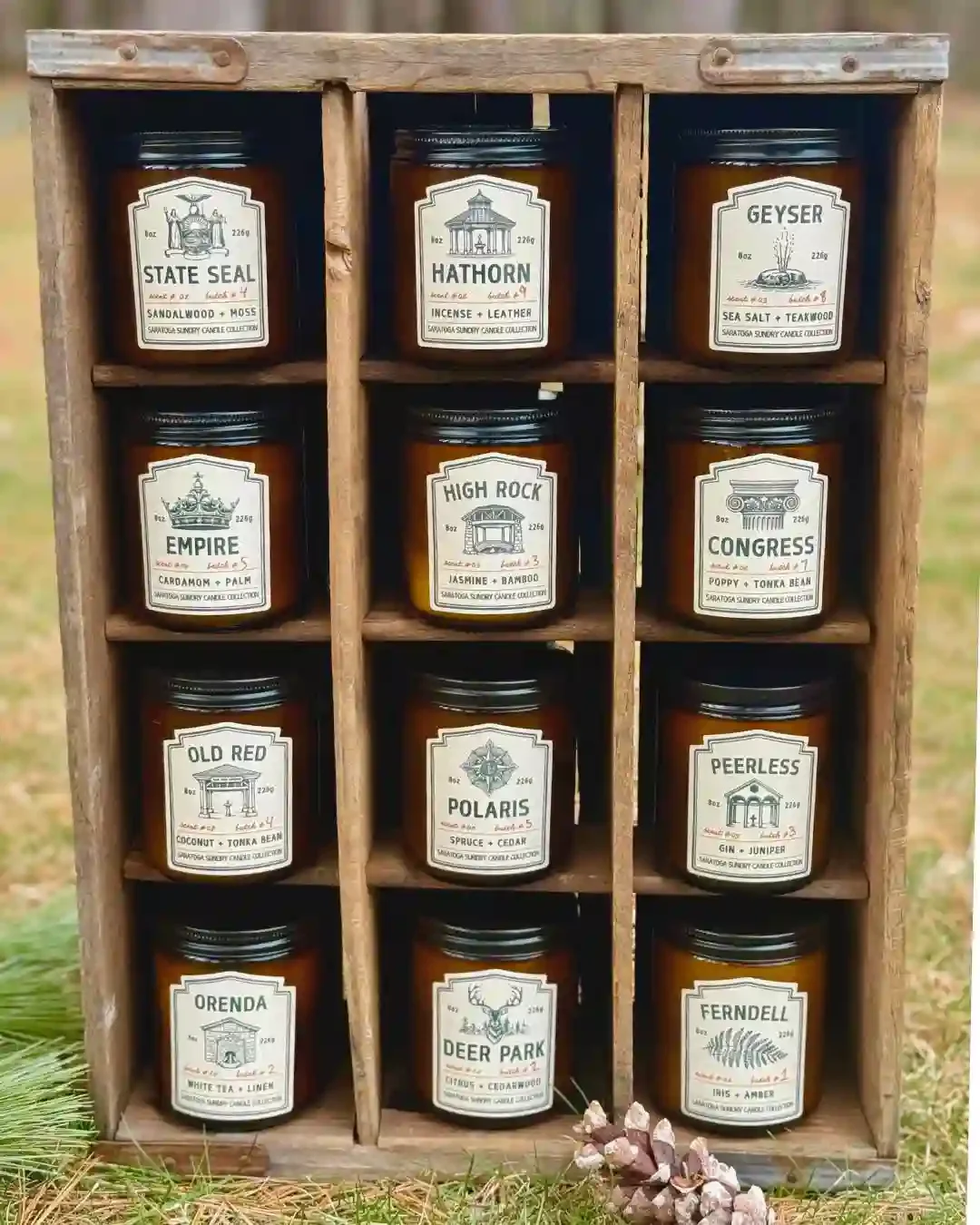 Collection of Saratoga Sundry joy candles in amber jars in wooden crate.webp