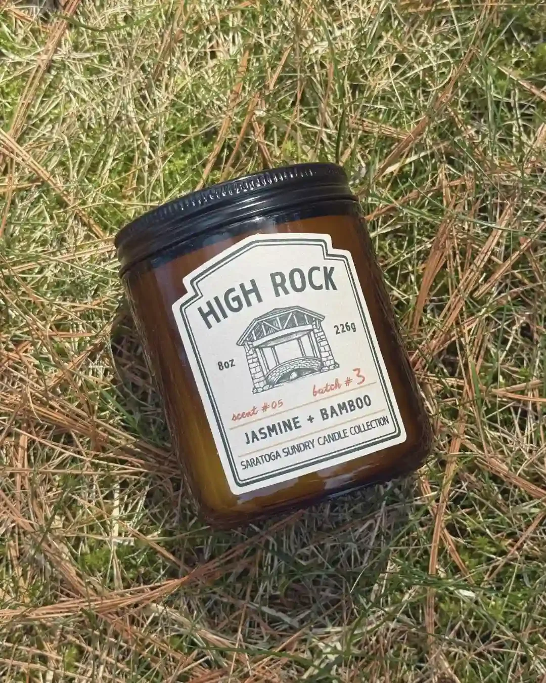 High Rock soy candle in amber jar from Saratoga Sundry laying in grass.webp