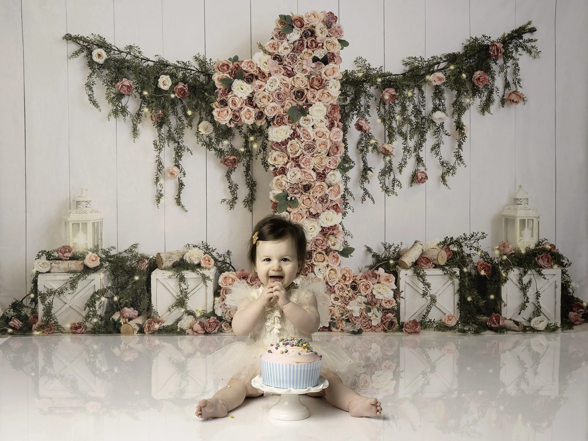 girl in ivory romper with a cake infant of her posing against floral 1 background