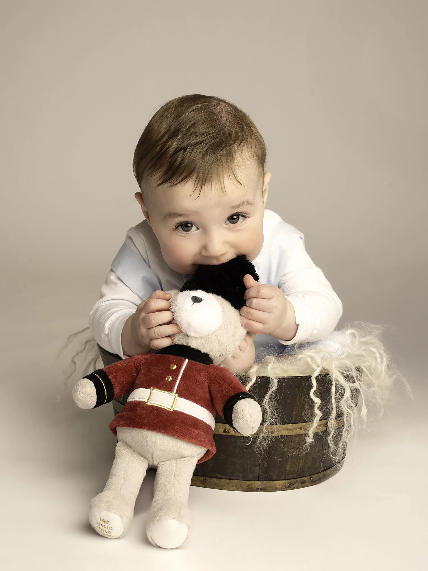 toddler biting on a teddy in a red jacket while  sitting in the  wooden bowl 
