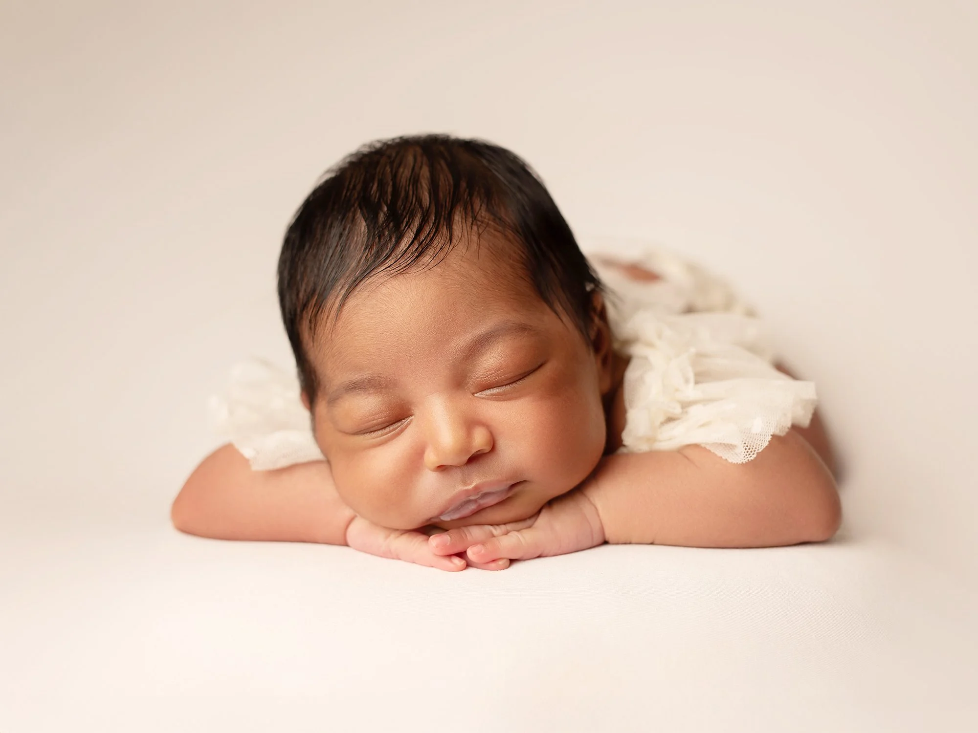 newborn baby in ivory outfit chin on hands pose