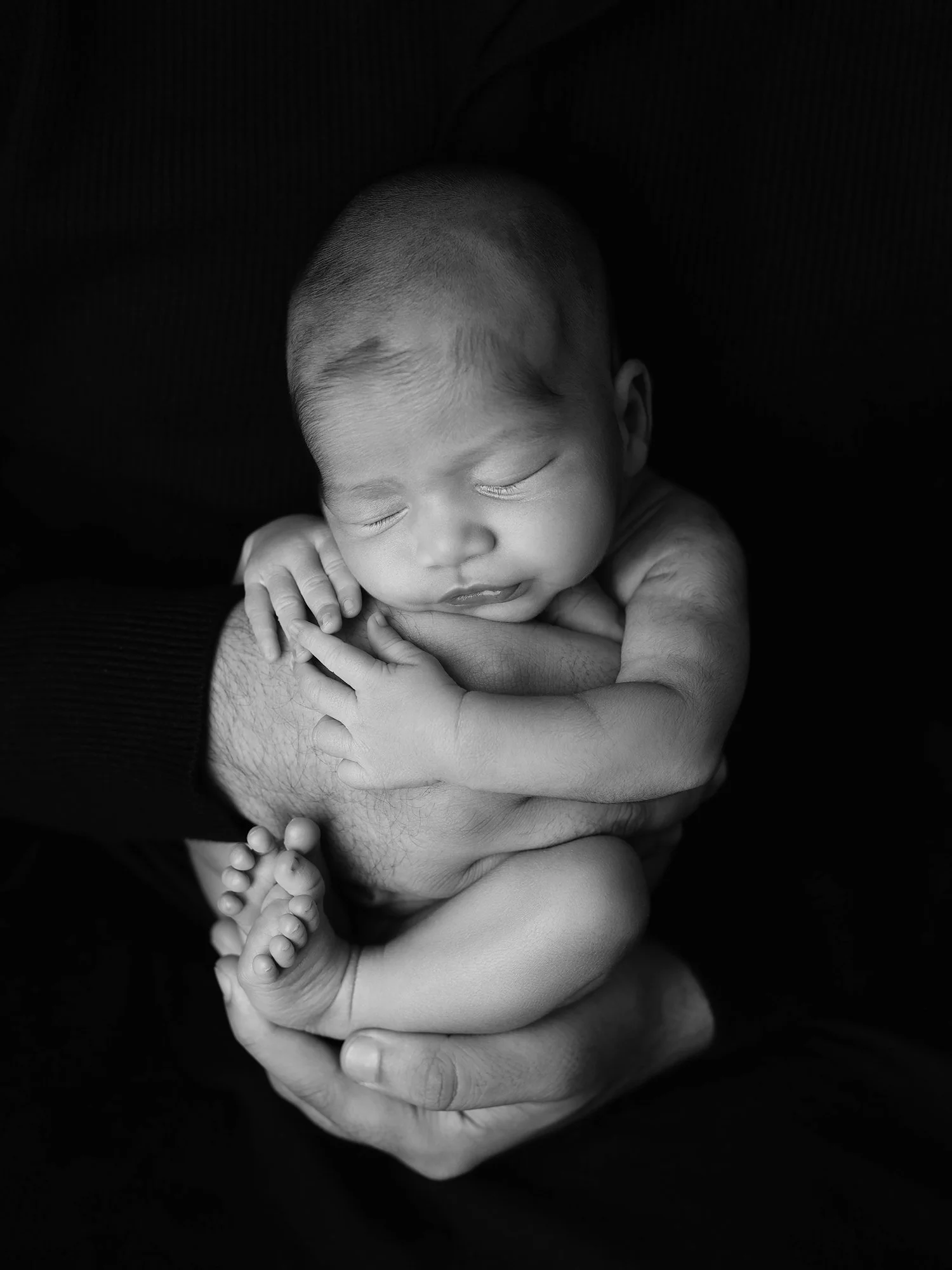 black and white picture of a newborn baby in fathers hands