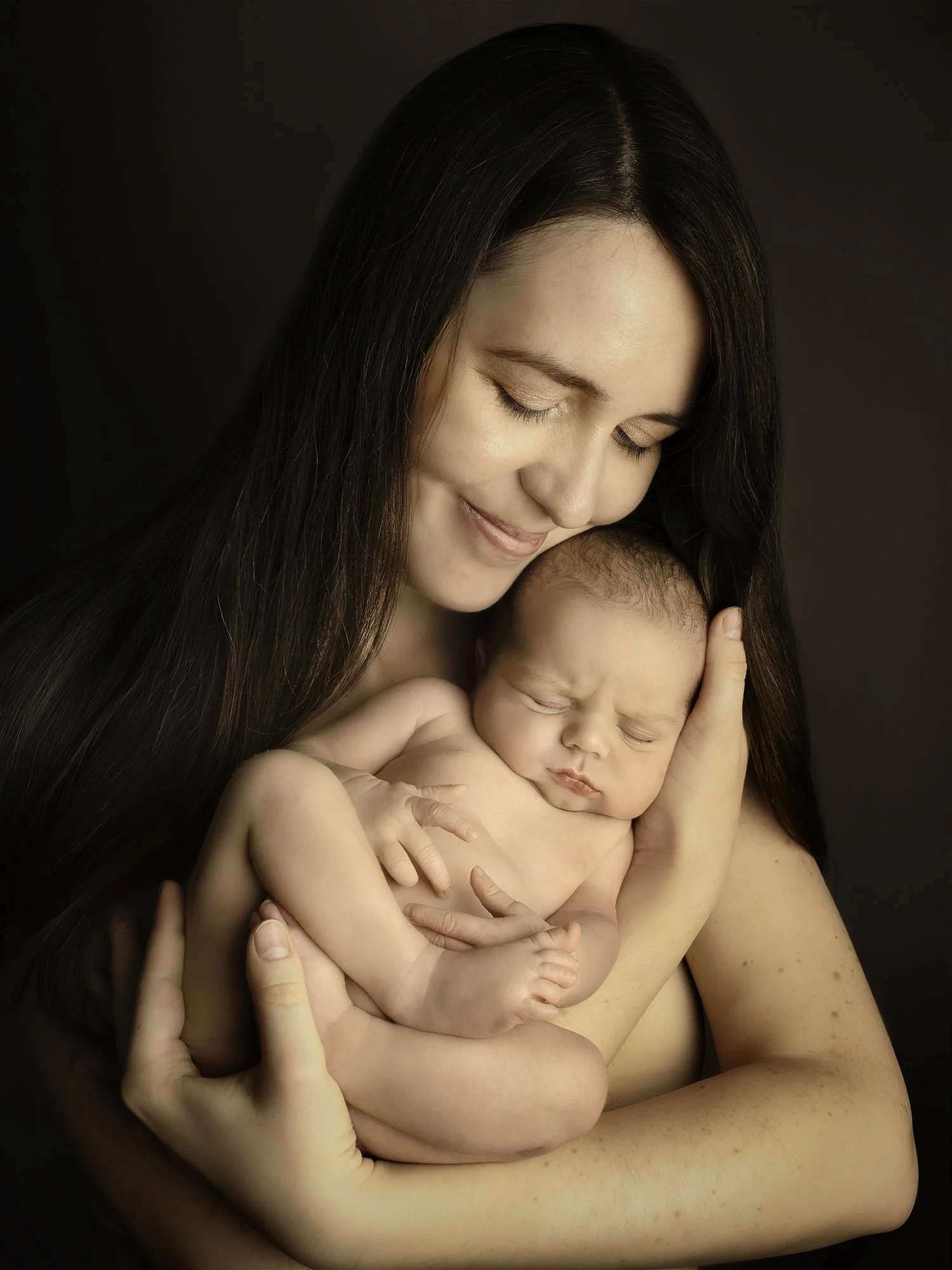 portrait image of a mother holding her newborn baby boy skin to skin