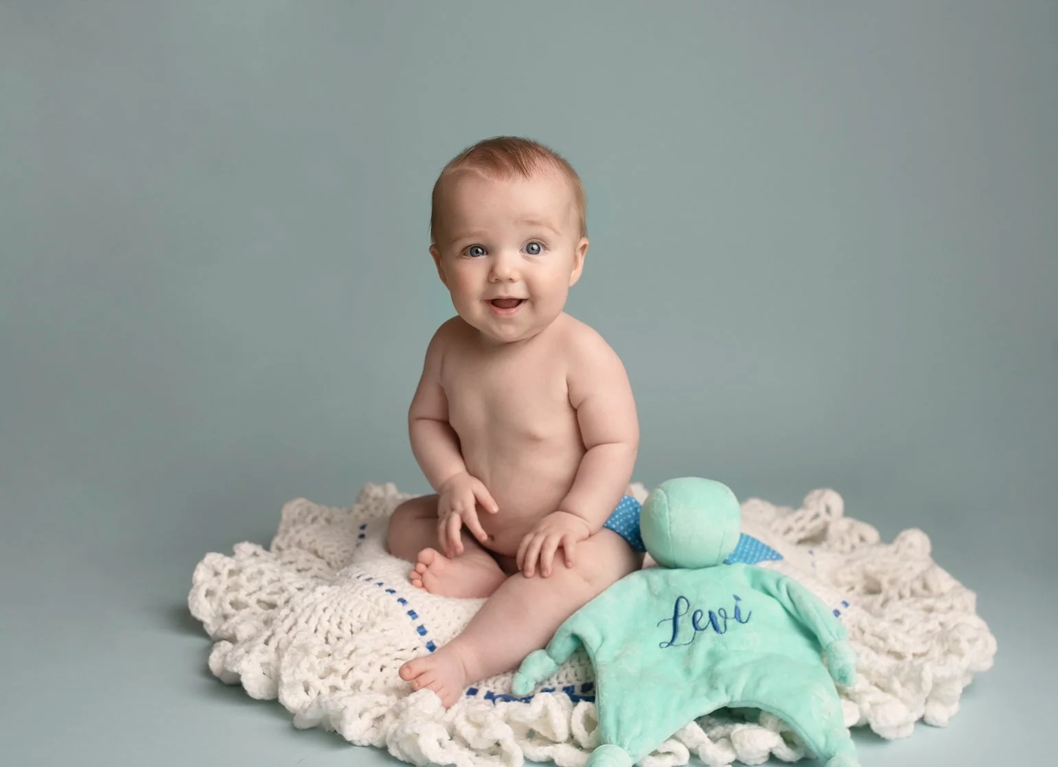 6 month old baby boy sitting on a crochet blanket with cuddle blue blanket 