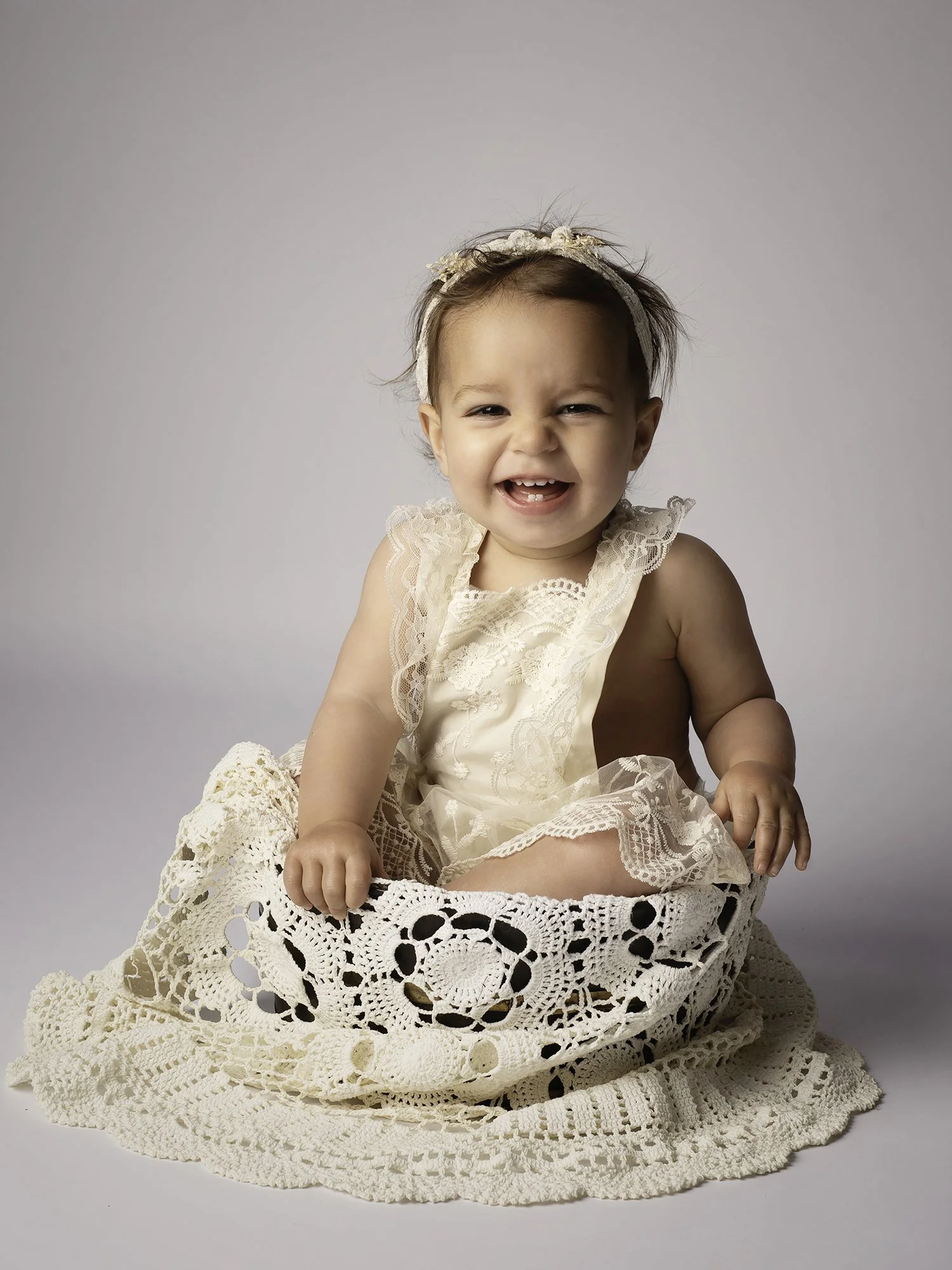 todler sitting in a bowl covered with ivory crochet blanket