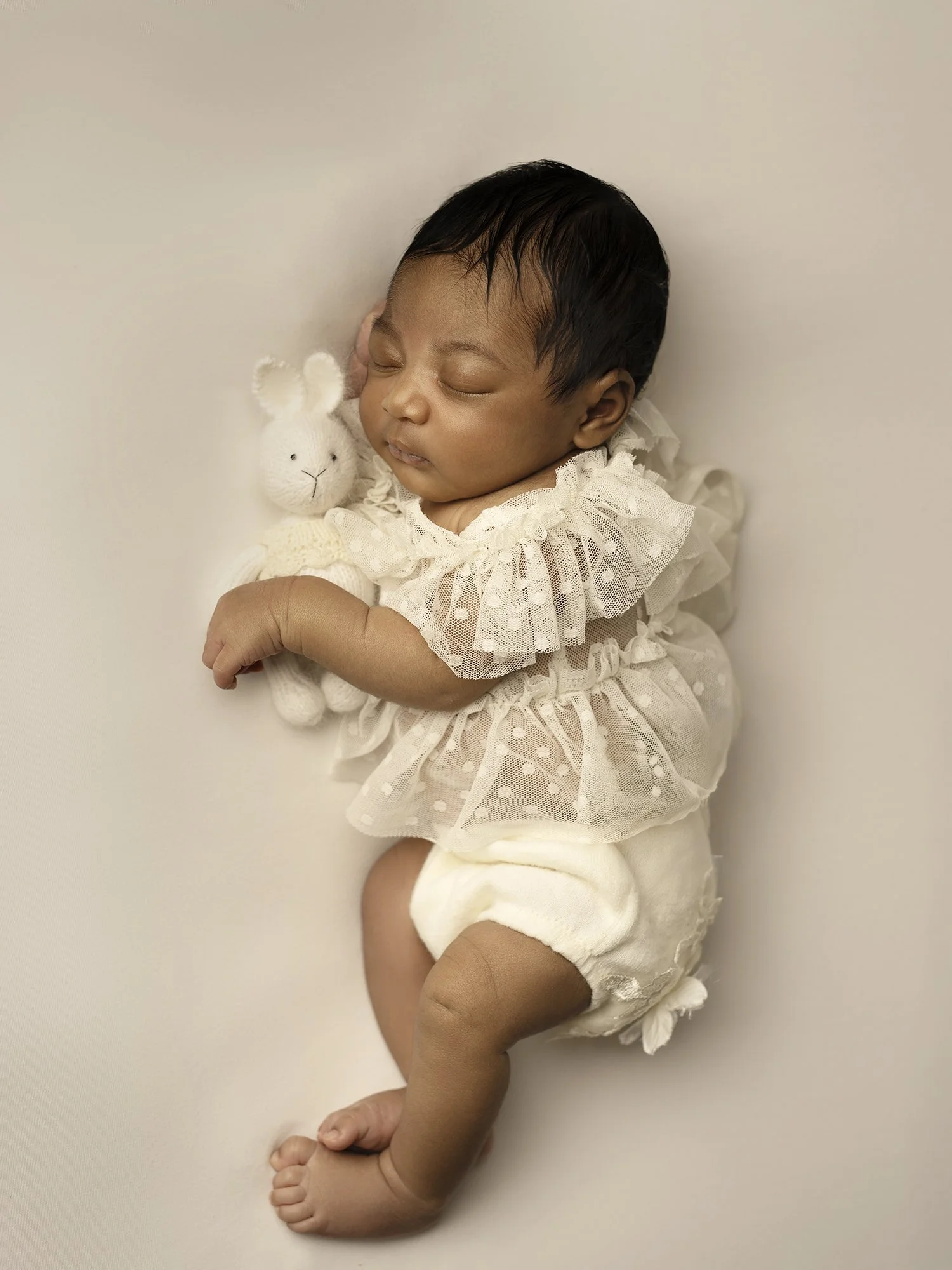 new baby in ivory outfit  side pose with a bunny toy