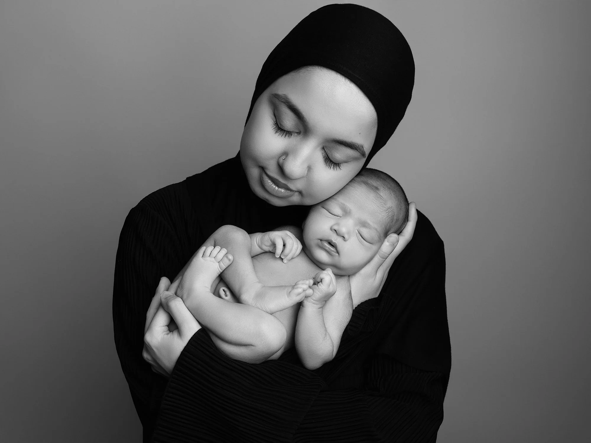 b7w picture of a woman in black  hijab holding her newborn child cheek to cheek