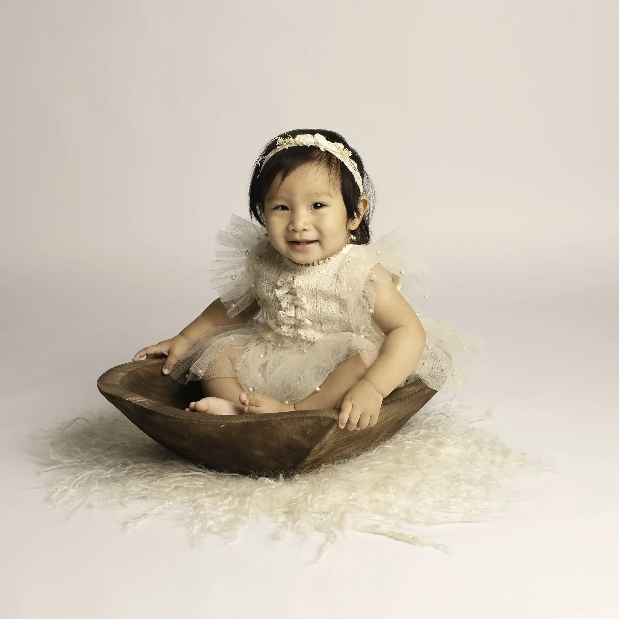 toddler is sitting in a wooden heart bowl posing against white backdrop