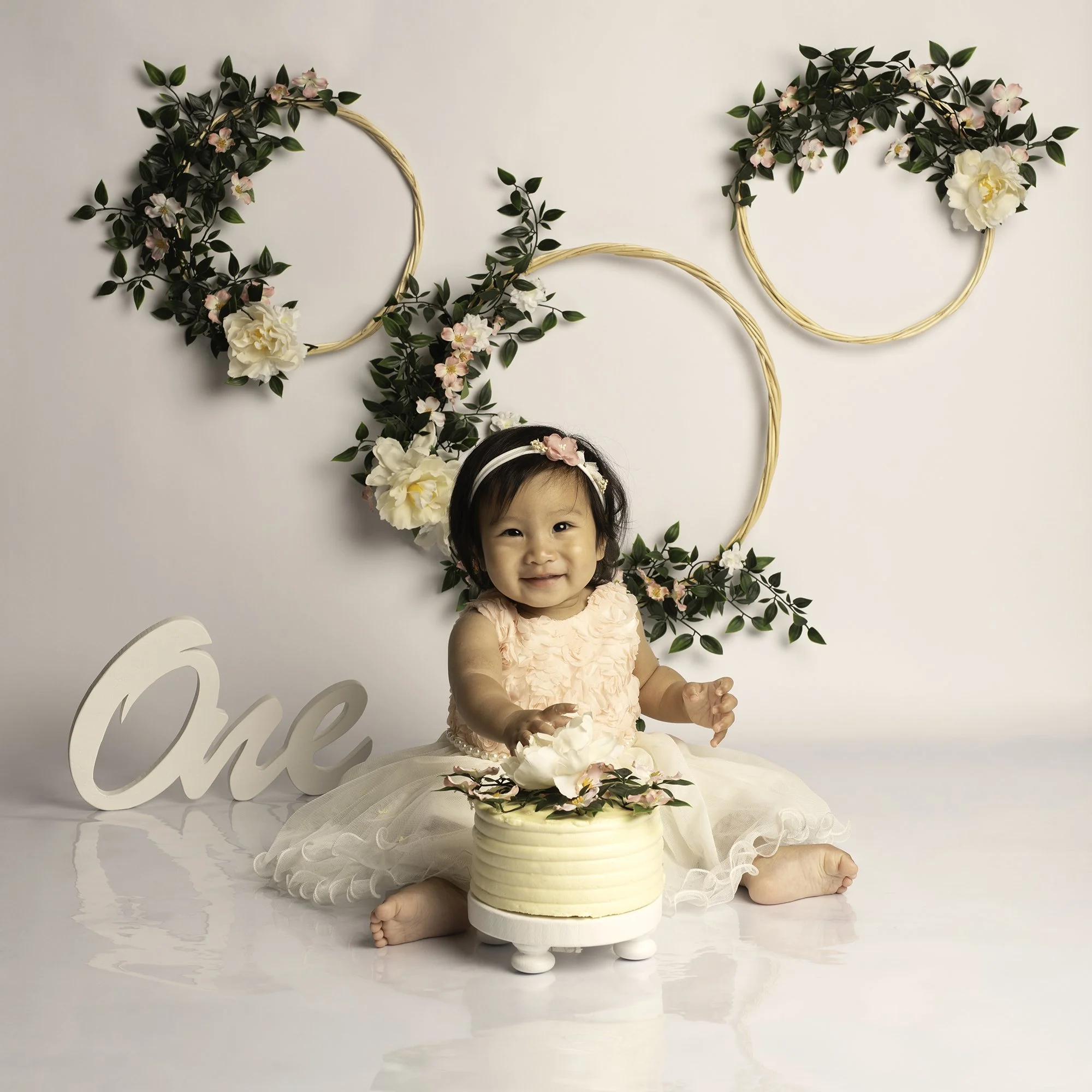 one year old girl with a cake infant of her with floral hoops background
