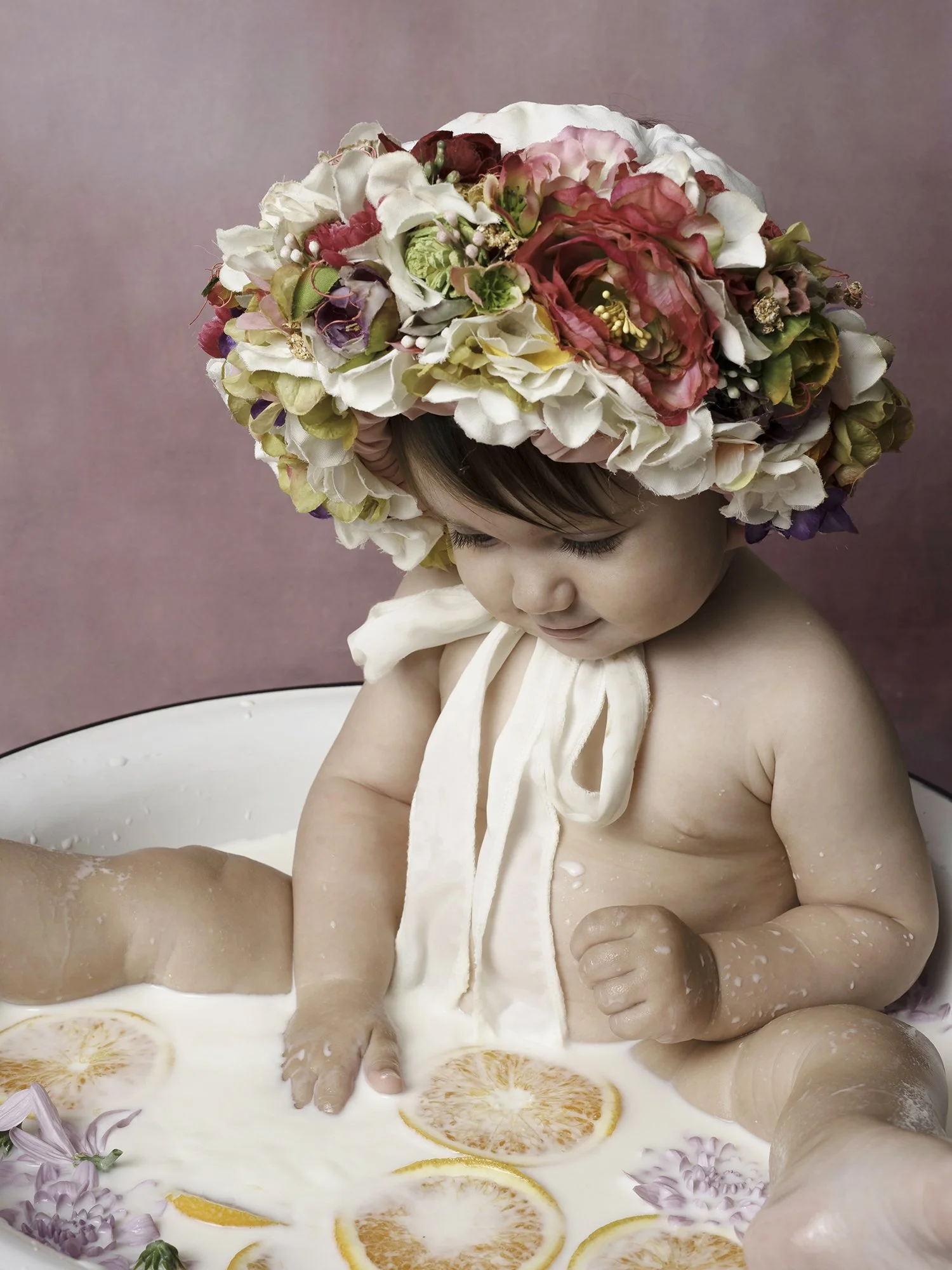 Baby in the bowl filled with milk, oranges and flowers