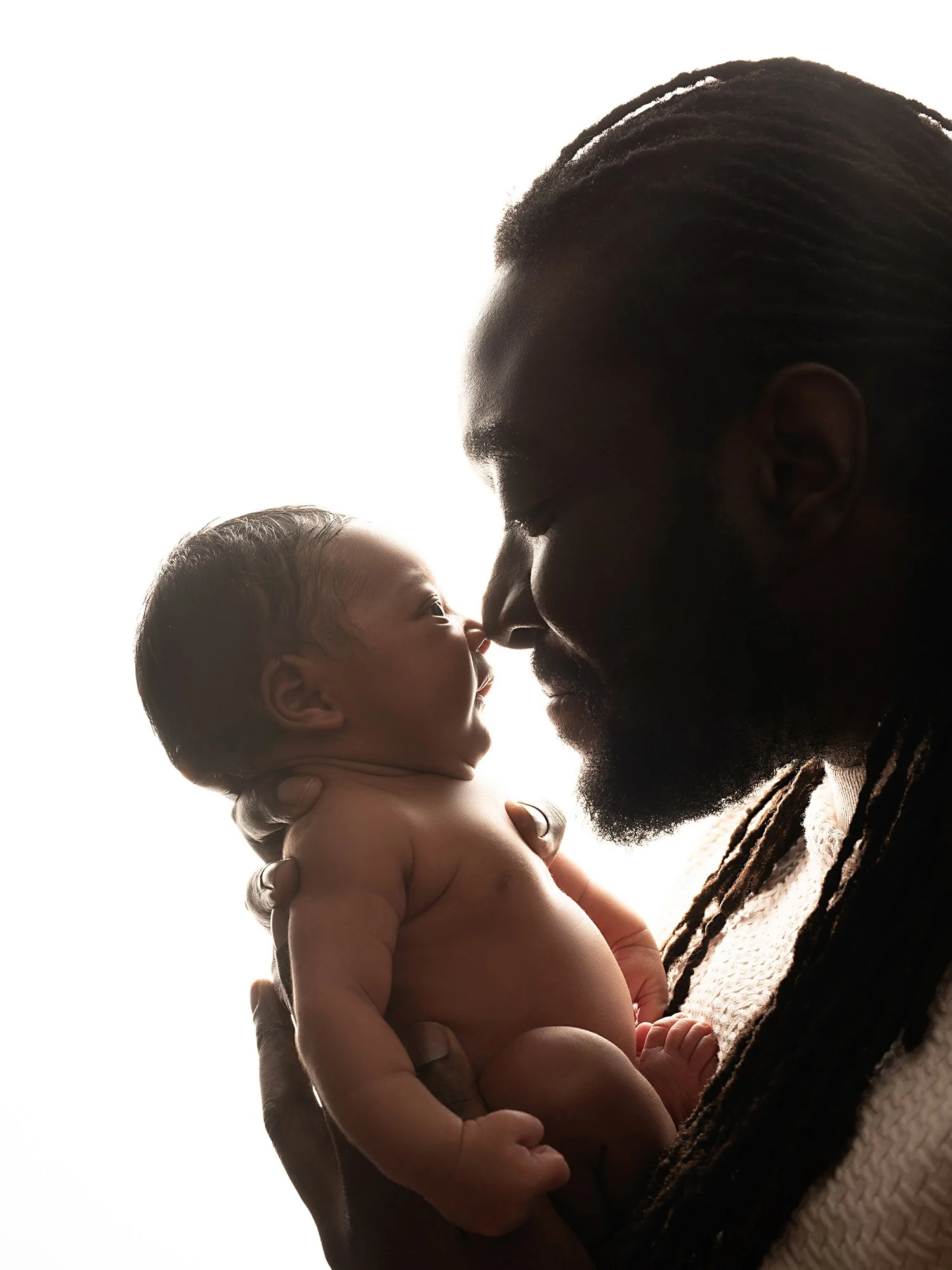 back lit  picture of a father holding his newborn baby nose to nose