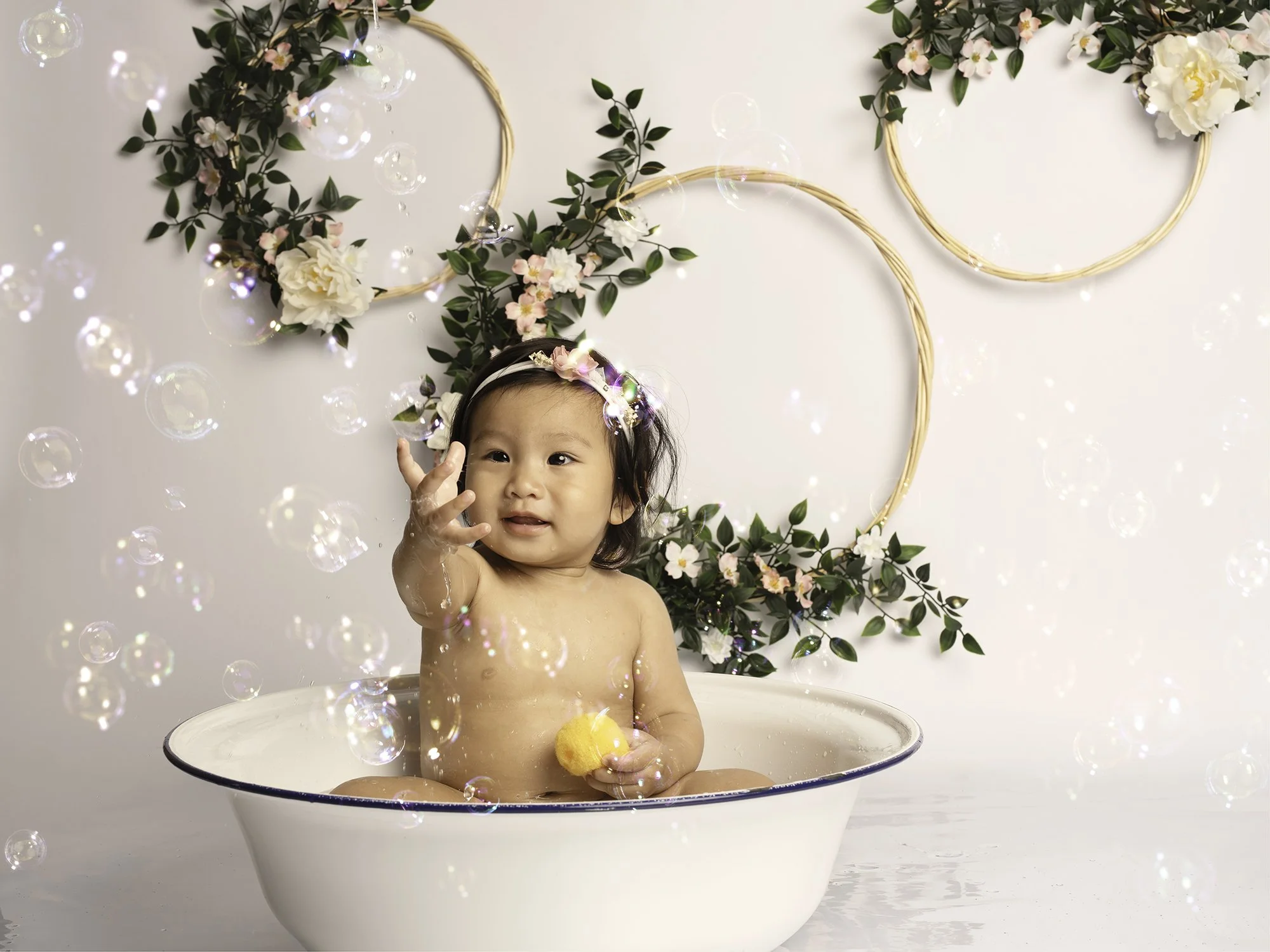 one year old in a vintage bowl first birthday bubbles and floral hoops at the background