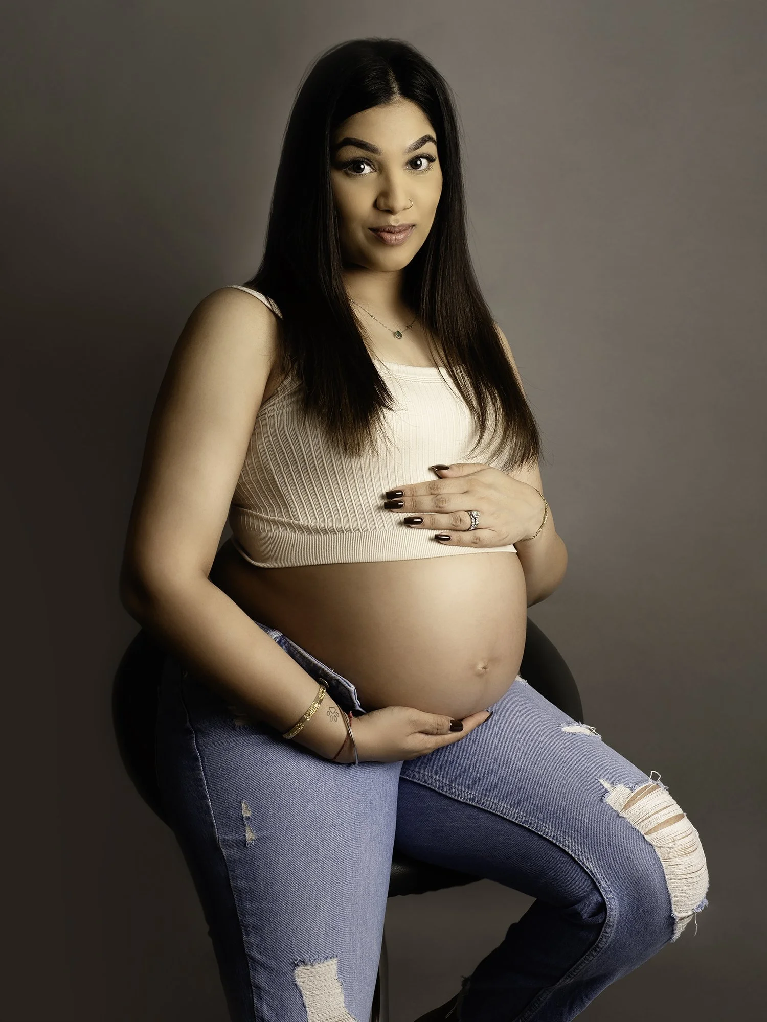 Pregnant woman denim jeans and crop t-shirt posing on the chair for a maternity photoshoot 