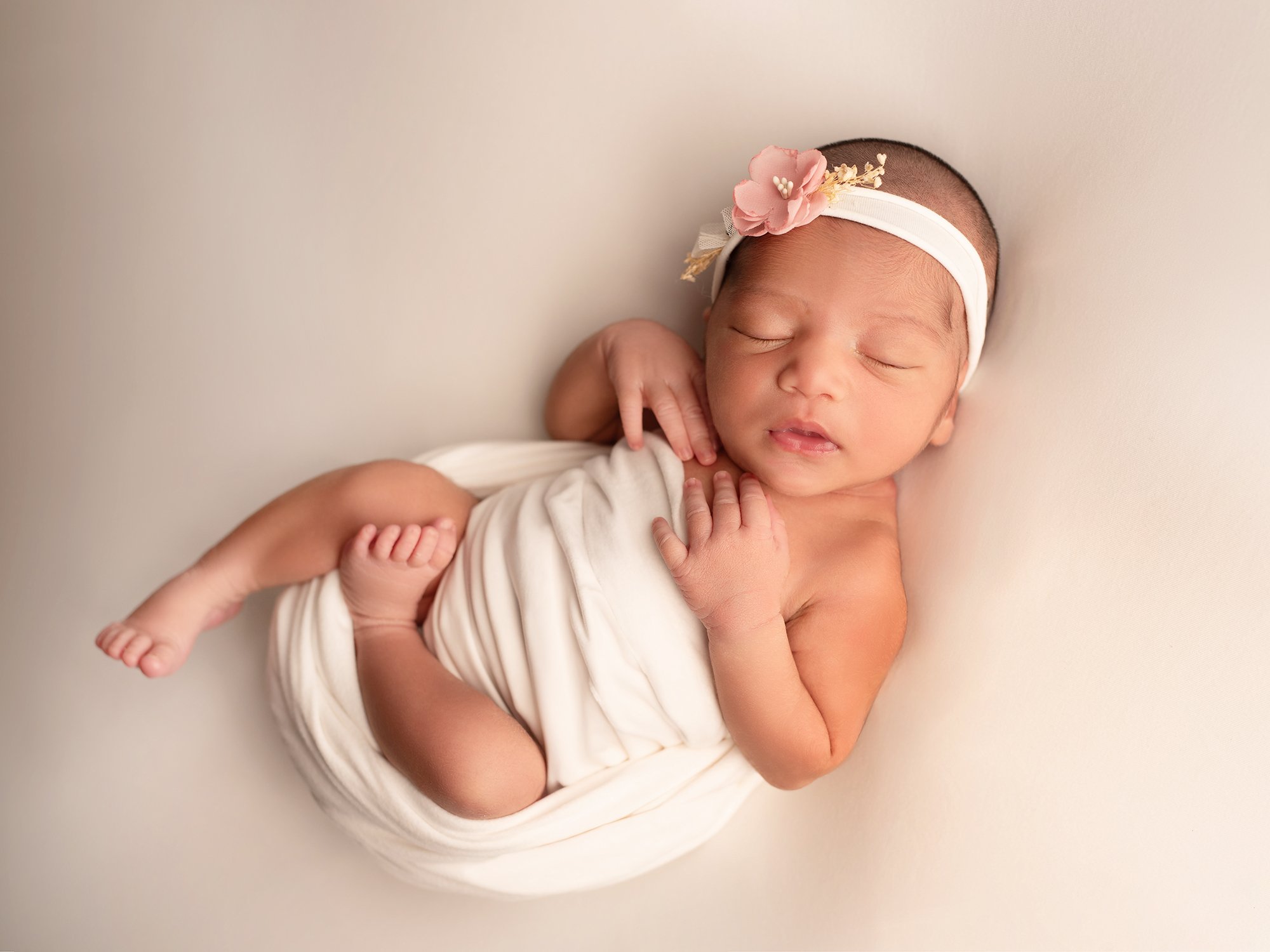 newborn baby wrapped in ivory stretch wrap agains a ivory background with a floral headband 