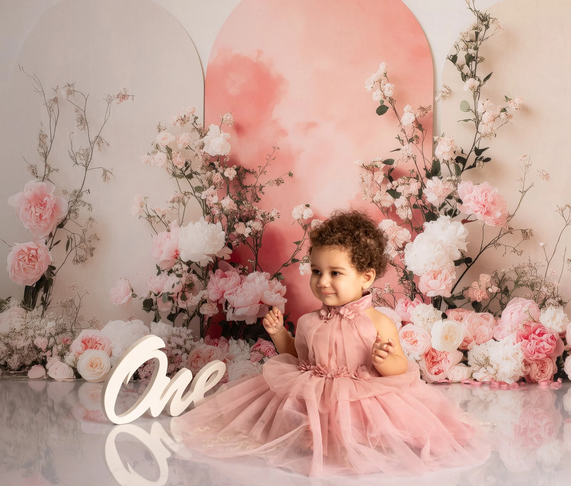 one year old child in a pink dress with floral background posing 