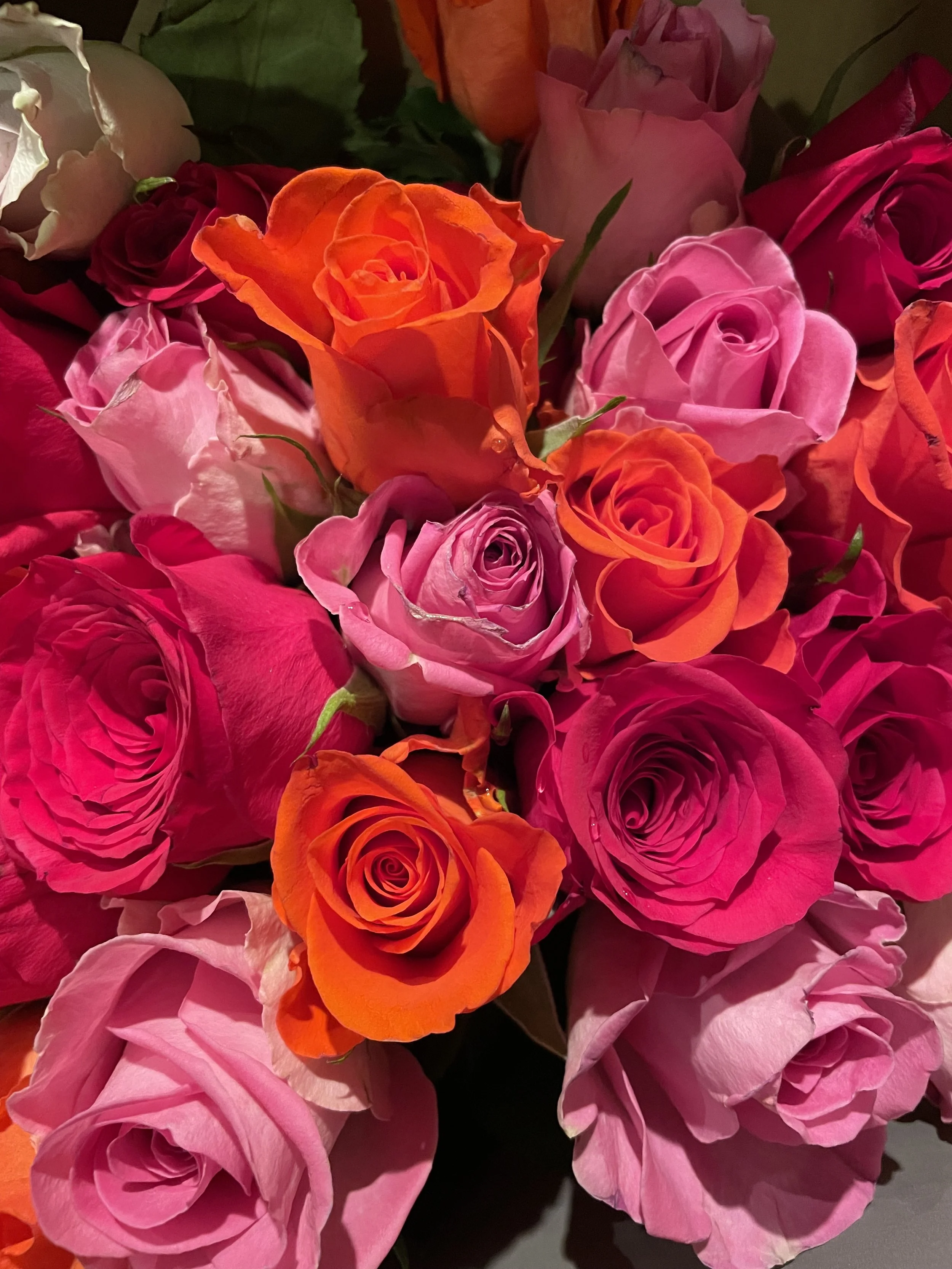 A bouquet of pink, orange, and white roses with lush green leaves.