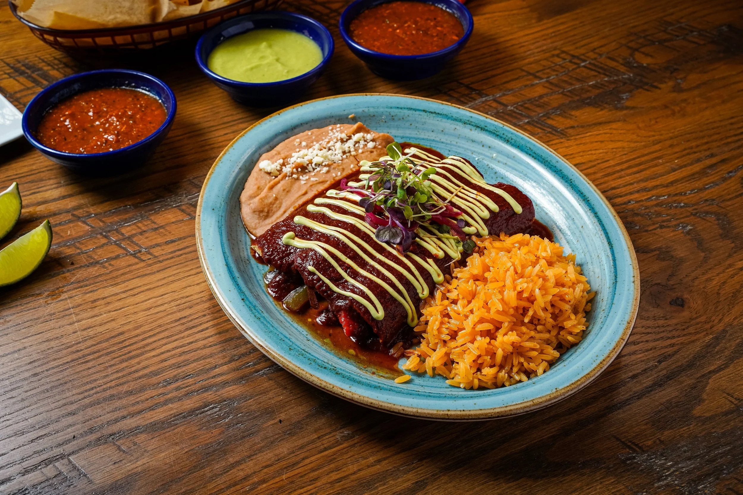 Plate of Mexican food with rice, beef or chicken fajita, and garnishes, with three bowls of salsa and guacamole on a wooden table.
