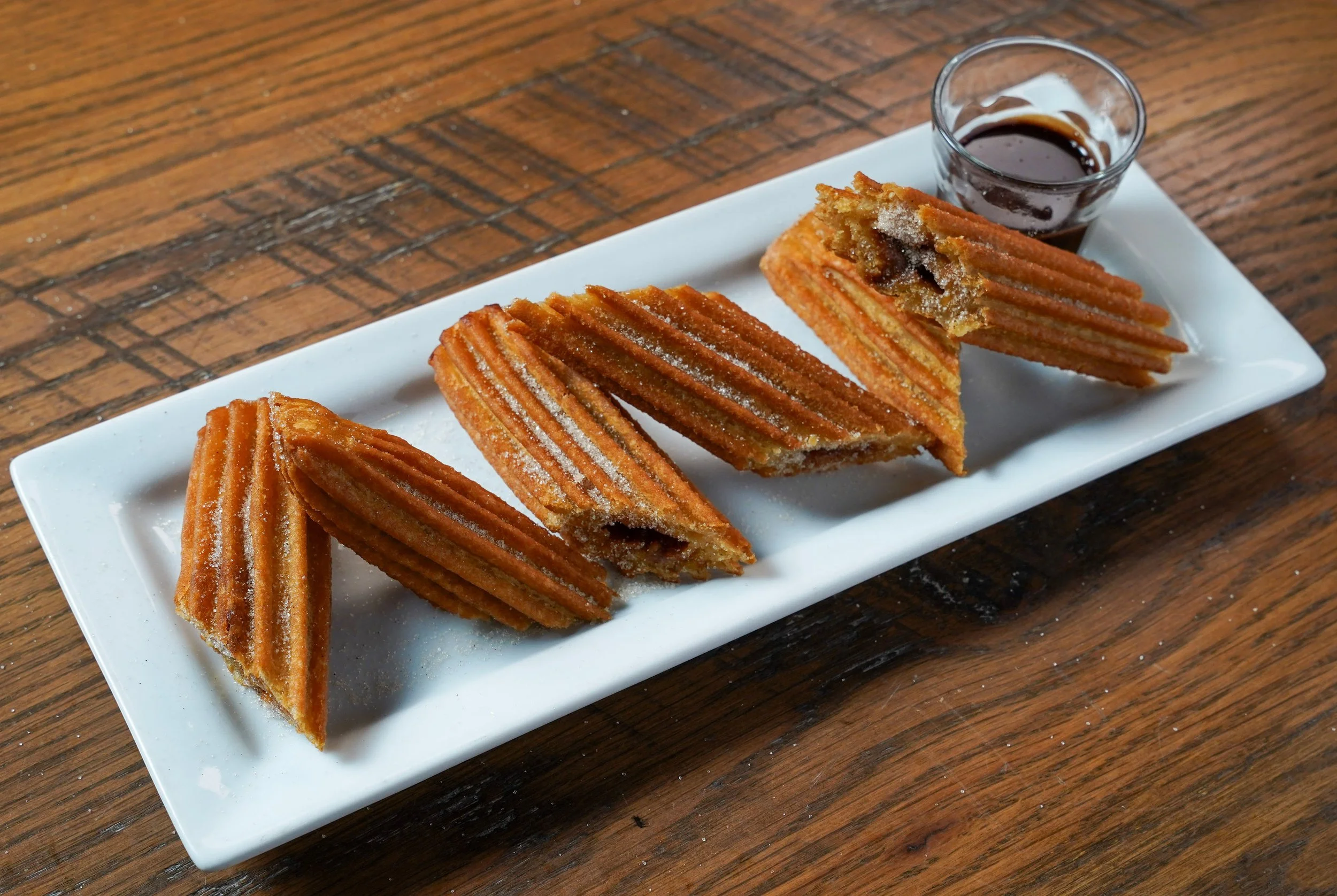 Churros with chocolate dipping sauce on a white rectangular plate."}#}\n