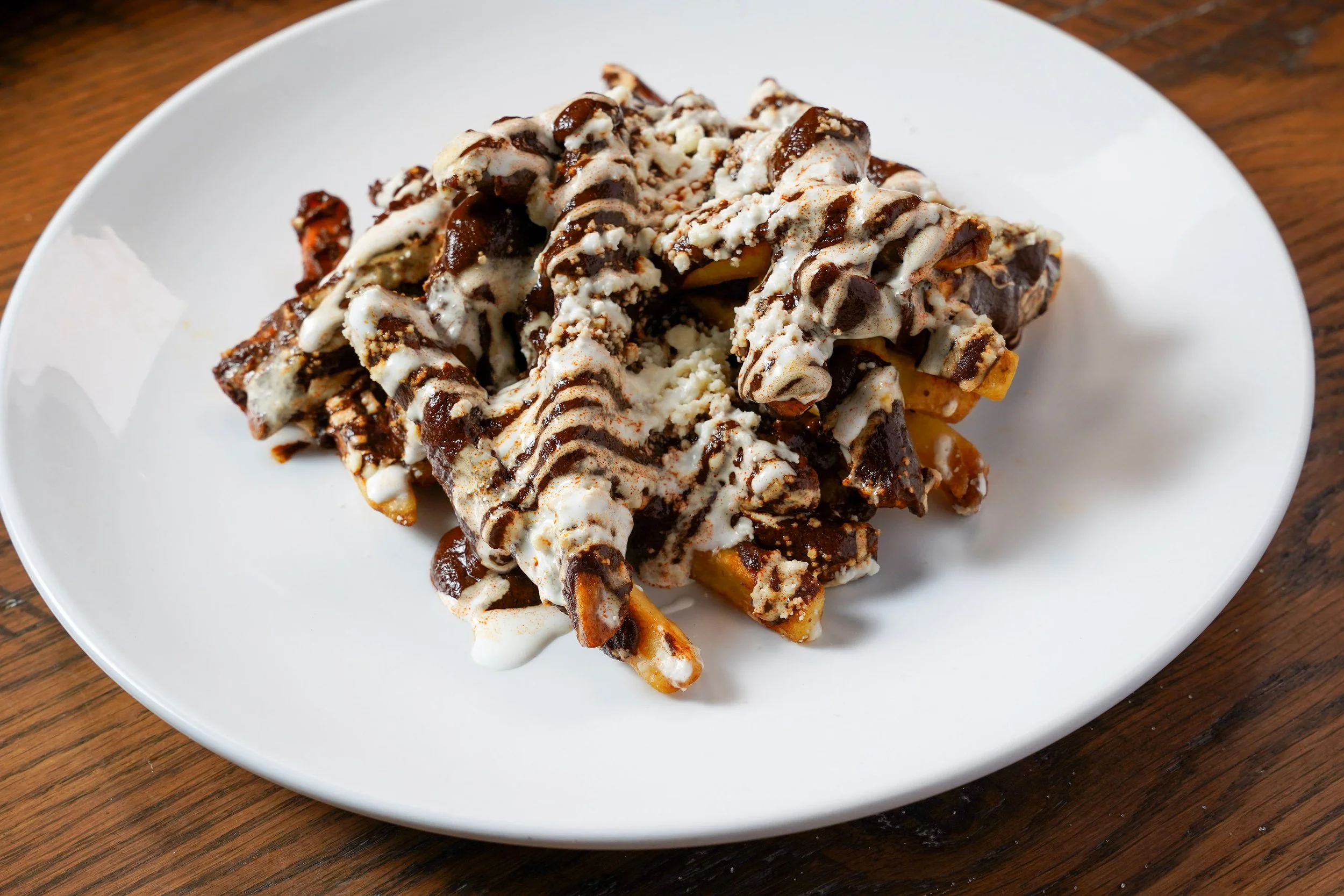 Plate of Belgian-style fries topped with melted cheese, chocolate sauce, and white drizzle.