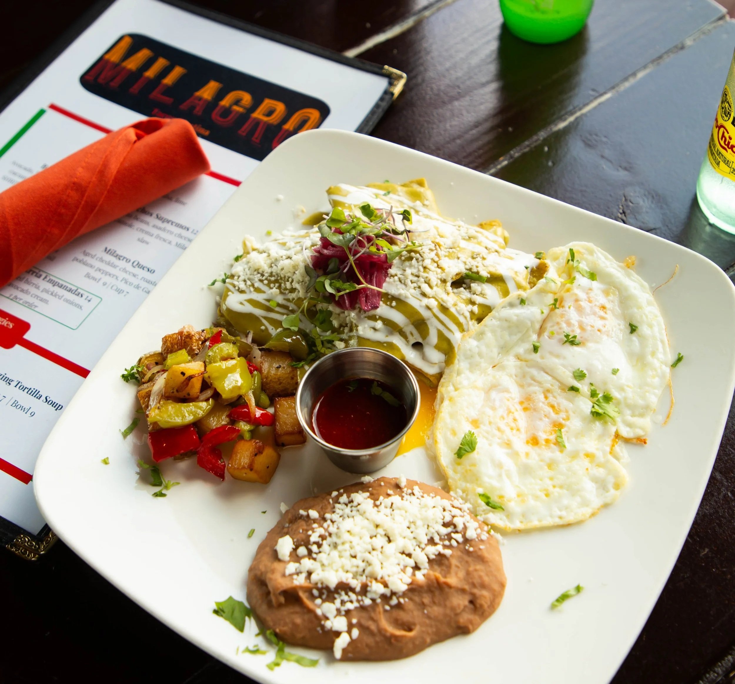 Plate of Mexican food with cheese, vegetables, and two fried eggs, served with salsa on the side. In the background, there is a menu with the word 'WILLACUDO' visible and a green drink container.