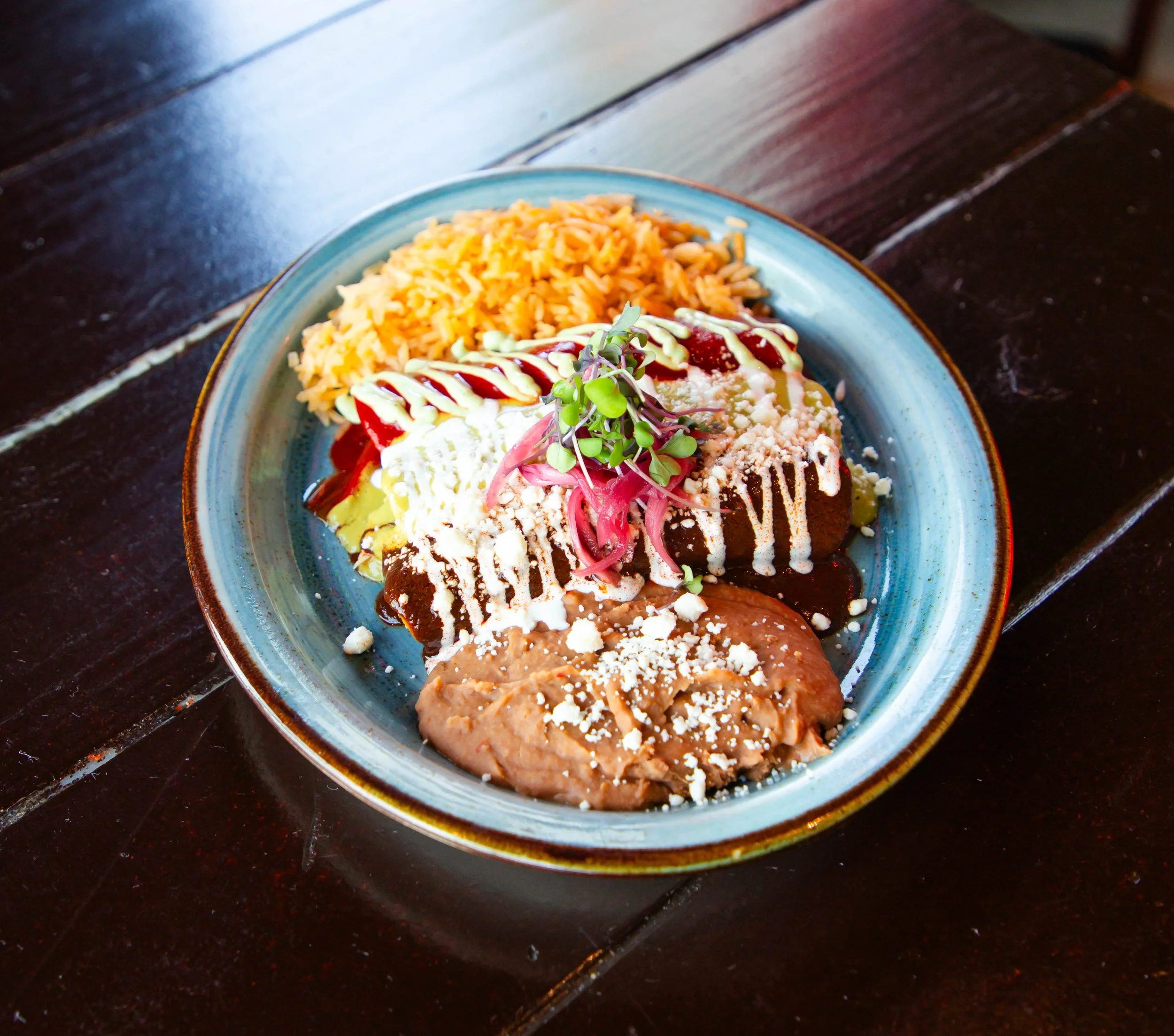 A dessert plate with rice pudding, decorated with shredded cheese, caramel sauce, whipped cream, and microgreens on top, served on a dark wooden table.