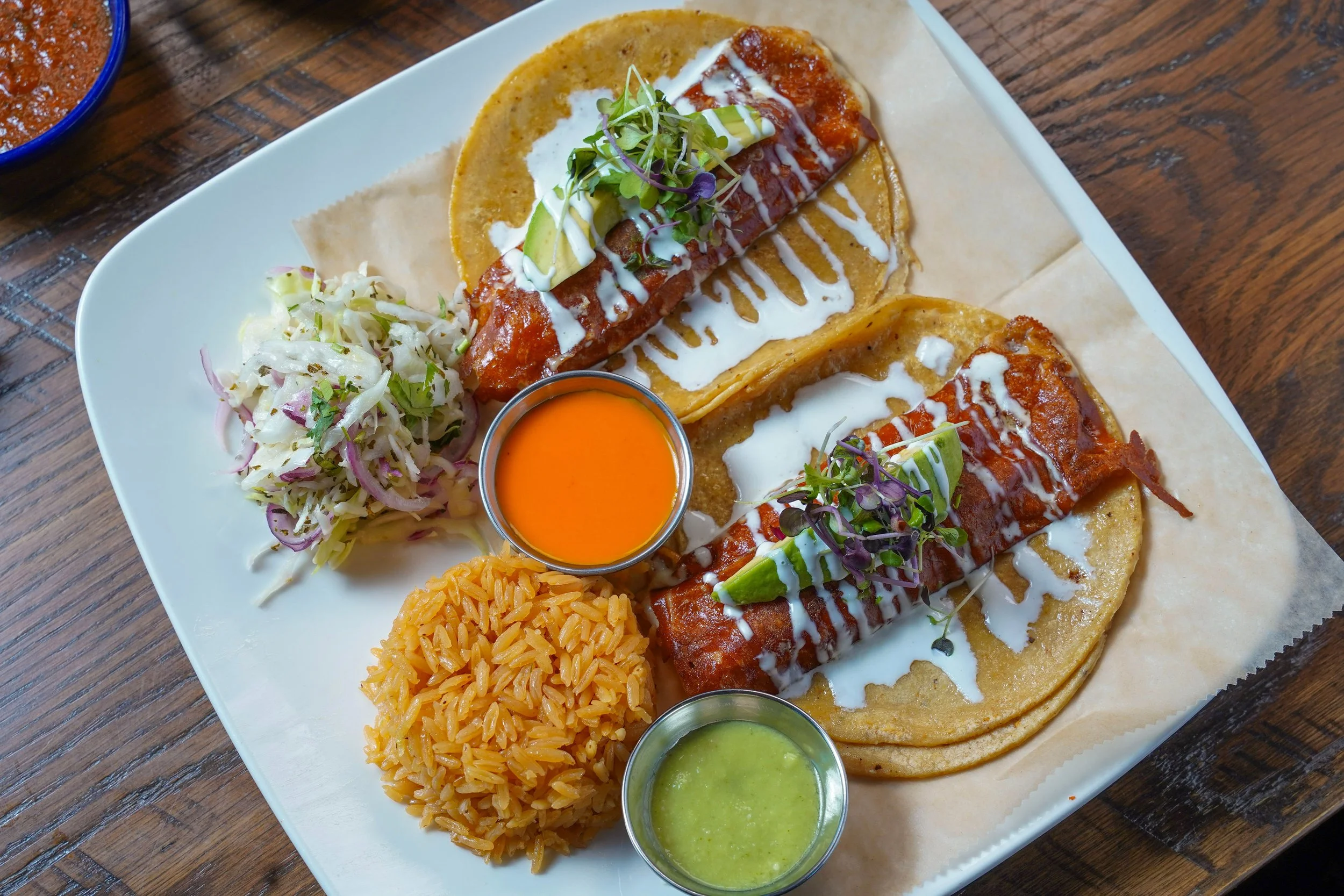 Plate of Mexican food including two tacos with meat and garnishes, Mexican rice, coleslaw, and various sauces.
