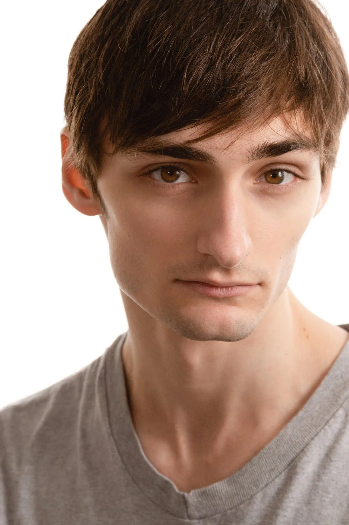 A young man with brown hair and brown eyes, wearing a gray shirt, looking directly at the camera against a white background.