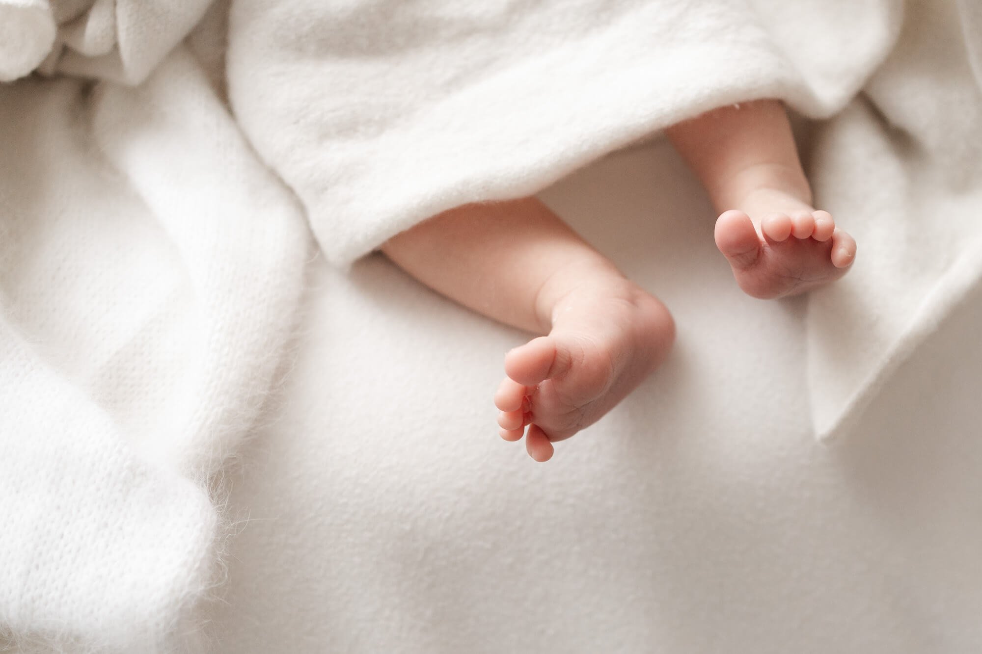 Detalle de los pies de un recién nacido sobre una manta blanca en casa