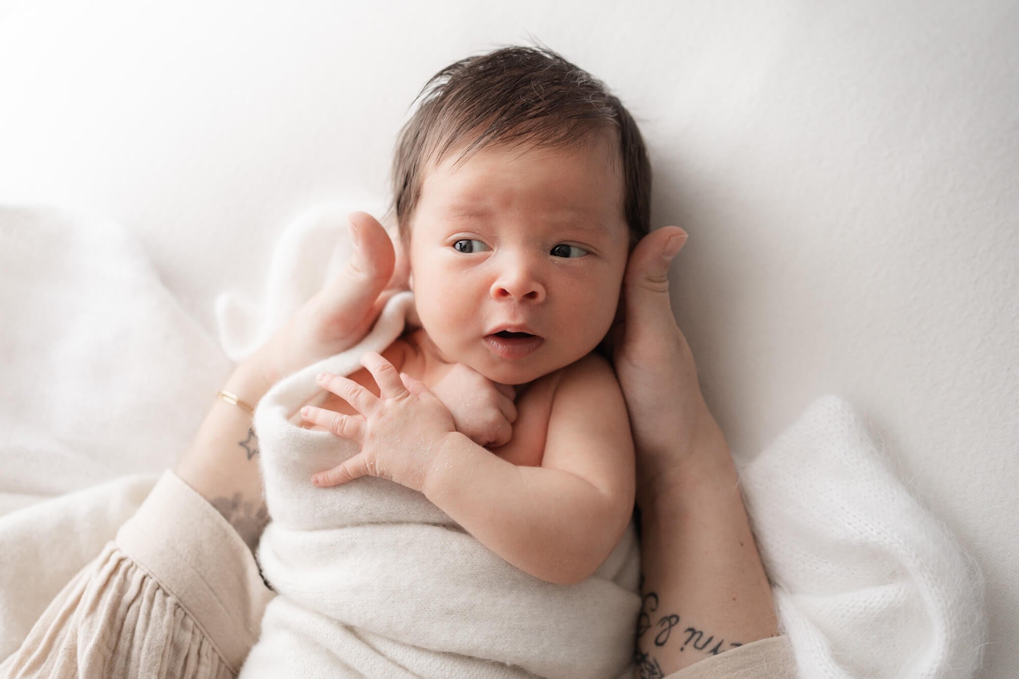 Bebé con ojos abiertos envuelto en manta blanca, durante una sesión newborn en Santander.