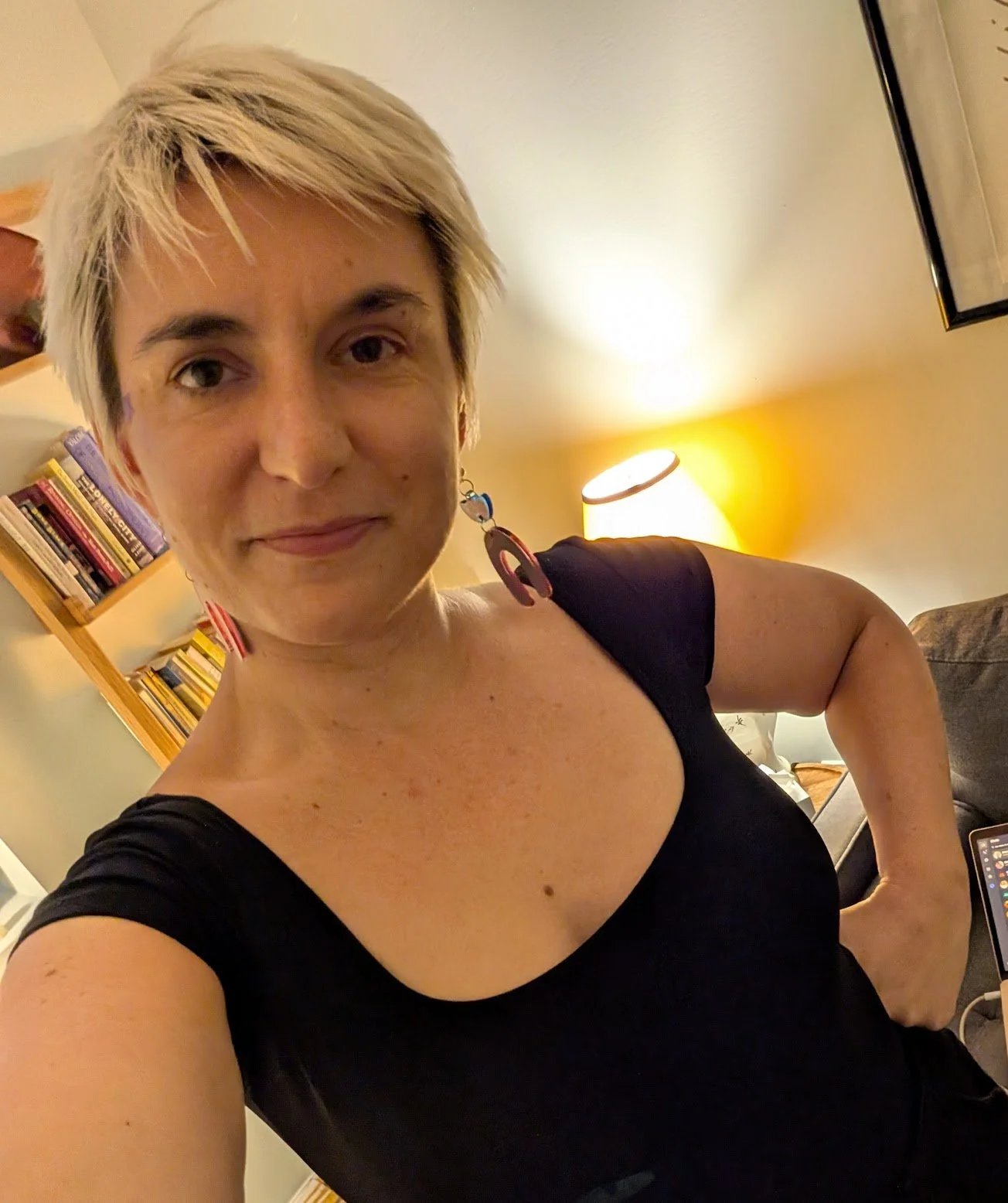 Image of a white, queer person with bleach blonde hair with a bookshelf in the background.