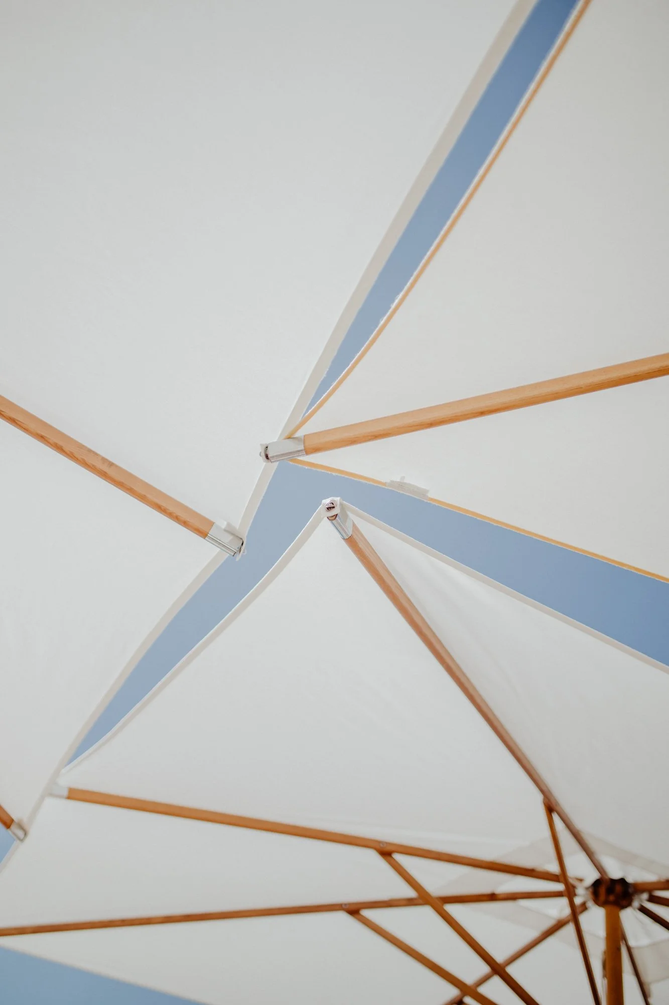 Close-up of white umbrellas with wooden frames against a pale blue sky.