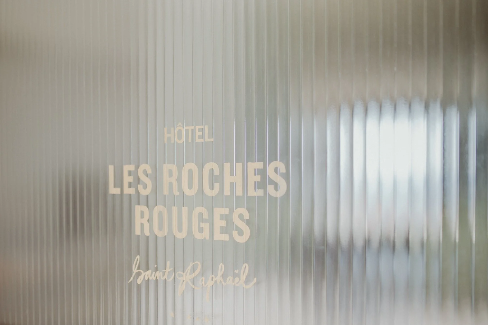 Hotel window with white text reading "HÔTEL LES ROCHES ROUGES Saint-Raphaël" on a frosted glass surface.