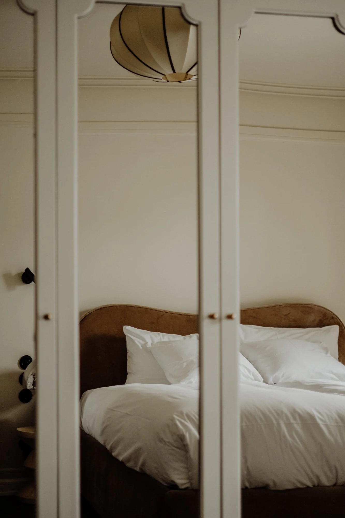 A bedroom with a bed, white bedding, and pillows seen through a sliding closet door with glass panels, and a ceiling light fixture.