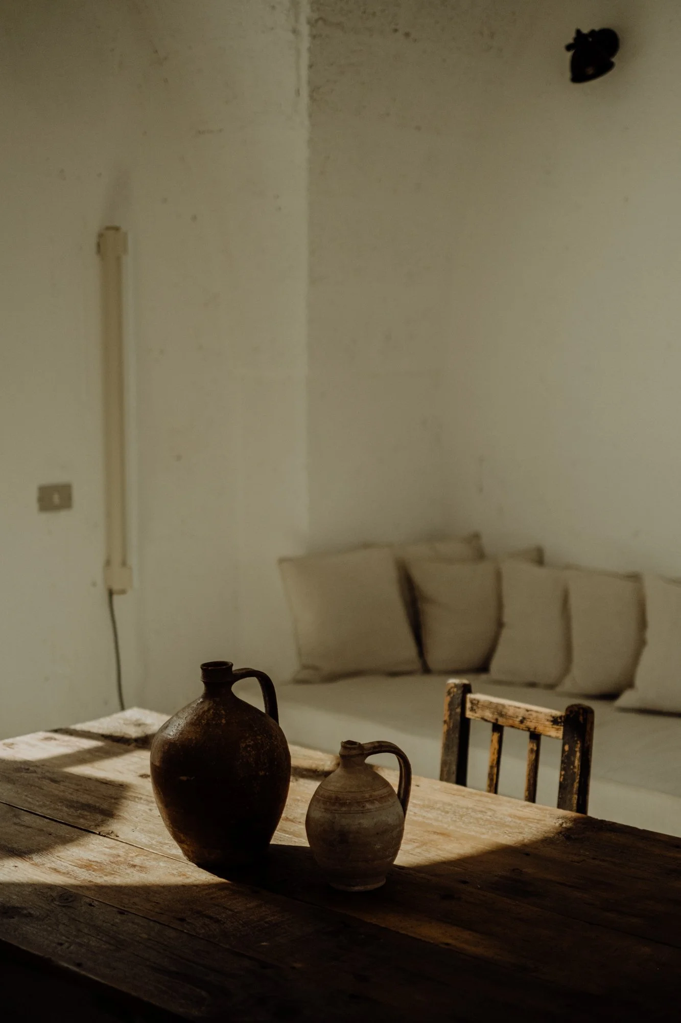 A rustic wooden table with two pottery vases, in a room with beige cushions on a white couch and a textured white wall in the background.