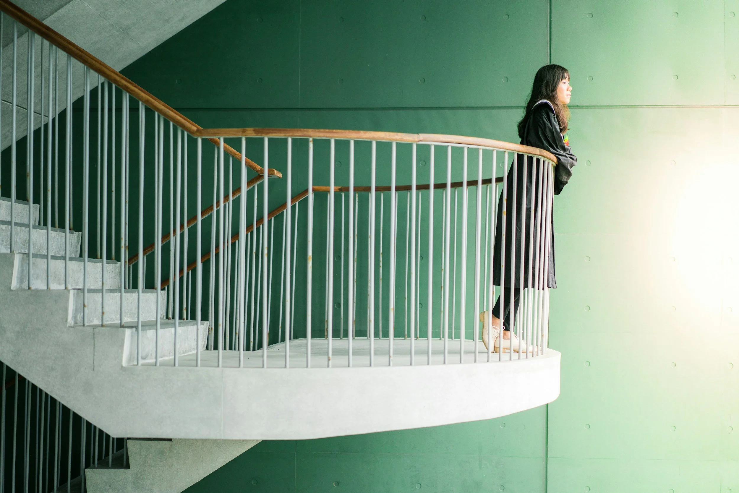 Woman standing on a staircase platform leaning on the railing and looking ahead