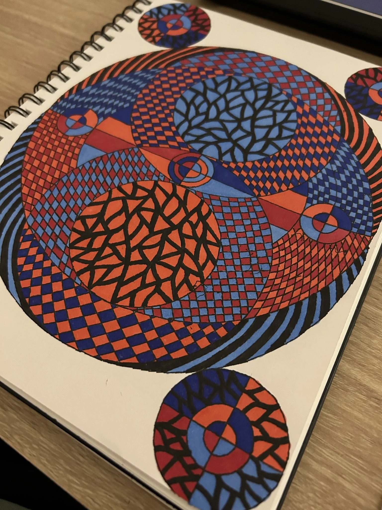 Colorful geometric pattern artwork featuring concentric circles, interwoven lines, and checkerboard and lattice patterns in red, blue, and black on white background.
