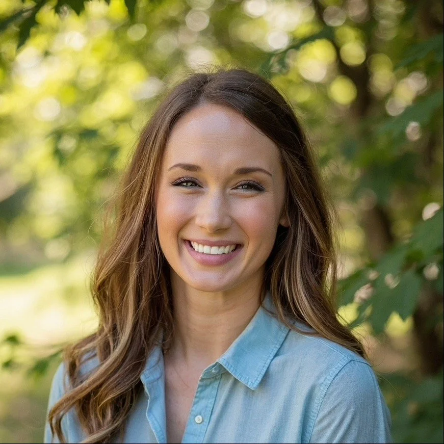 Tara Garrett - COO of Refuge Roofing with long brown hair smiling outdoors in front of green trees