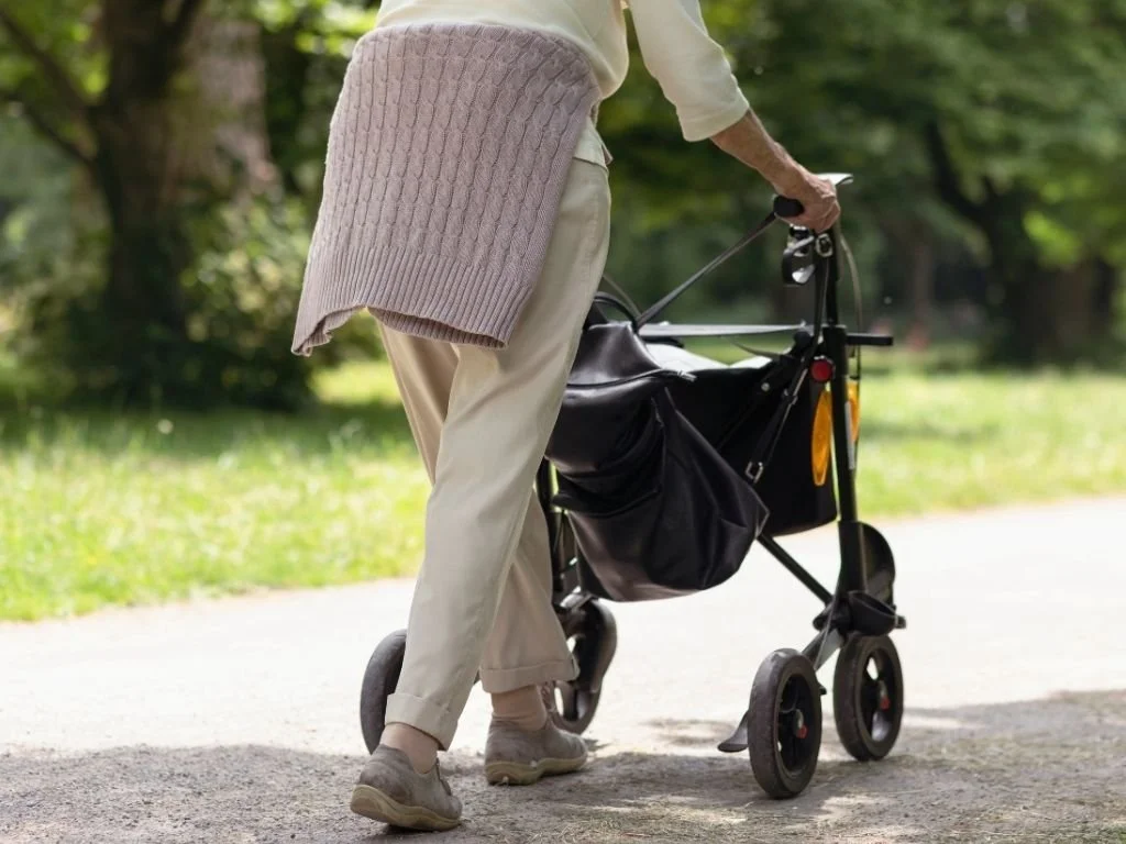 Persona mayor caminando con un andador en un parque verde.