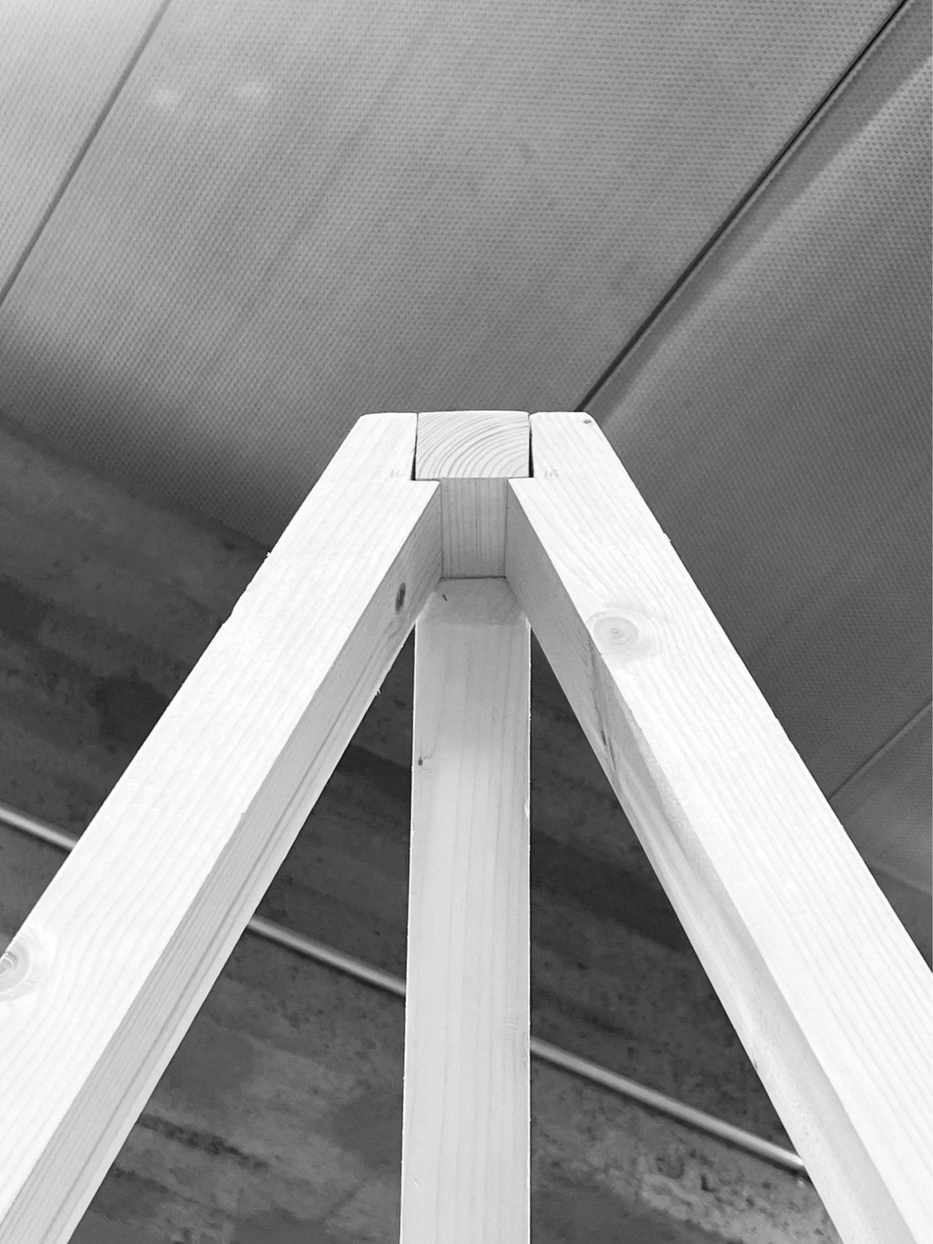 Close-up of the top corner of a wooden A-frame ladder against a metallic ceiling.