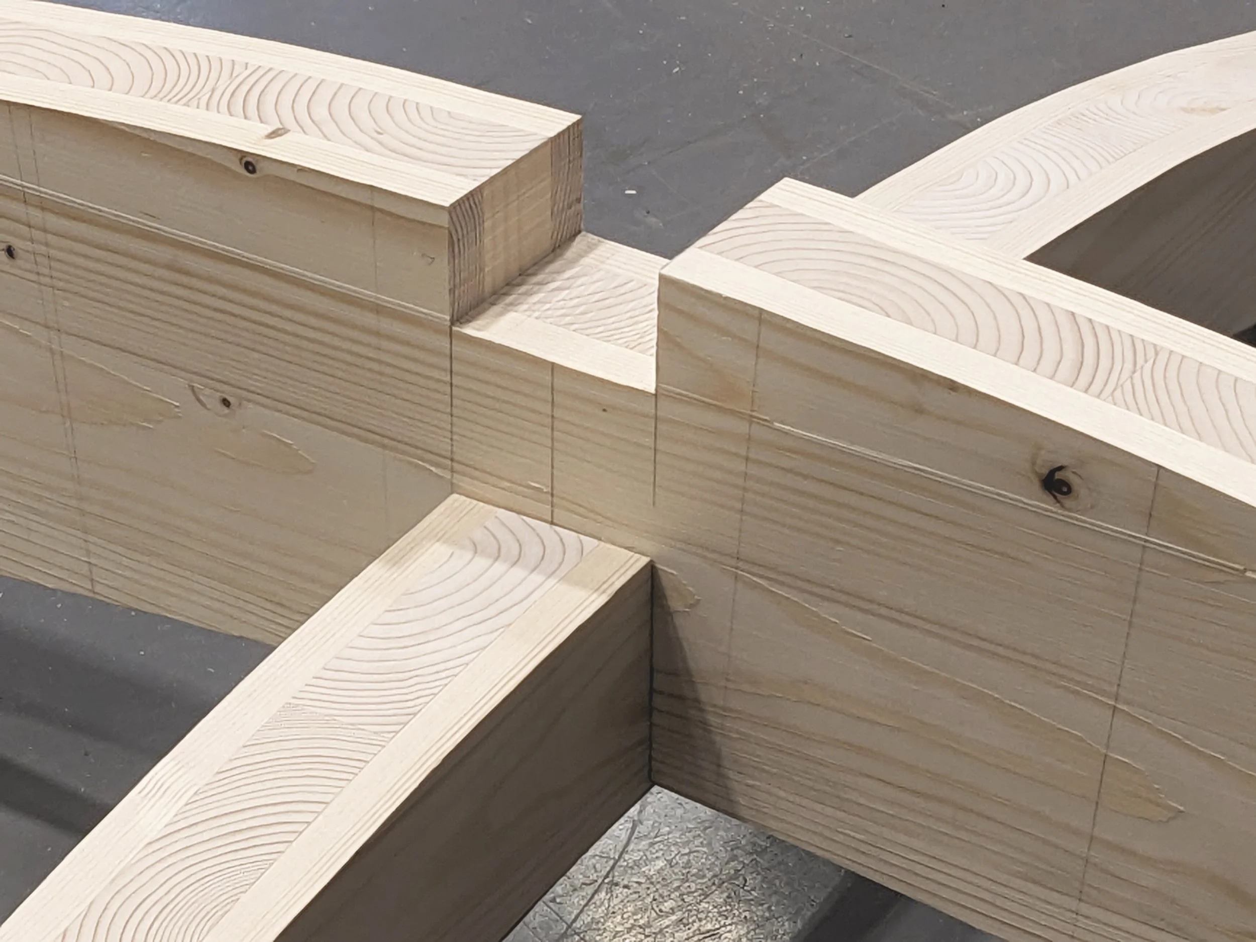 Close-up view of wooden beams with visible grain patterns, joined together on a workbench, likely in the process of construction or woodworking.