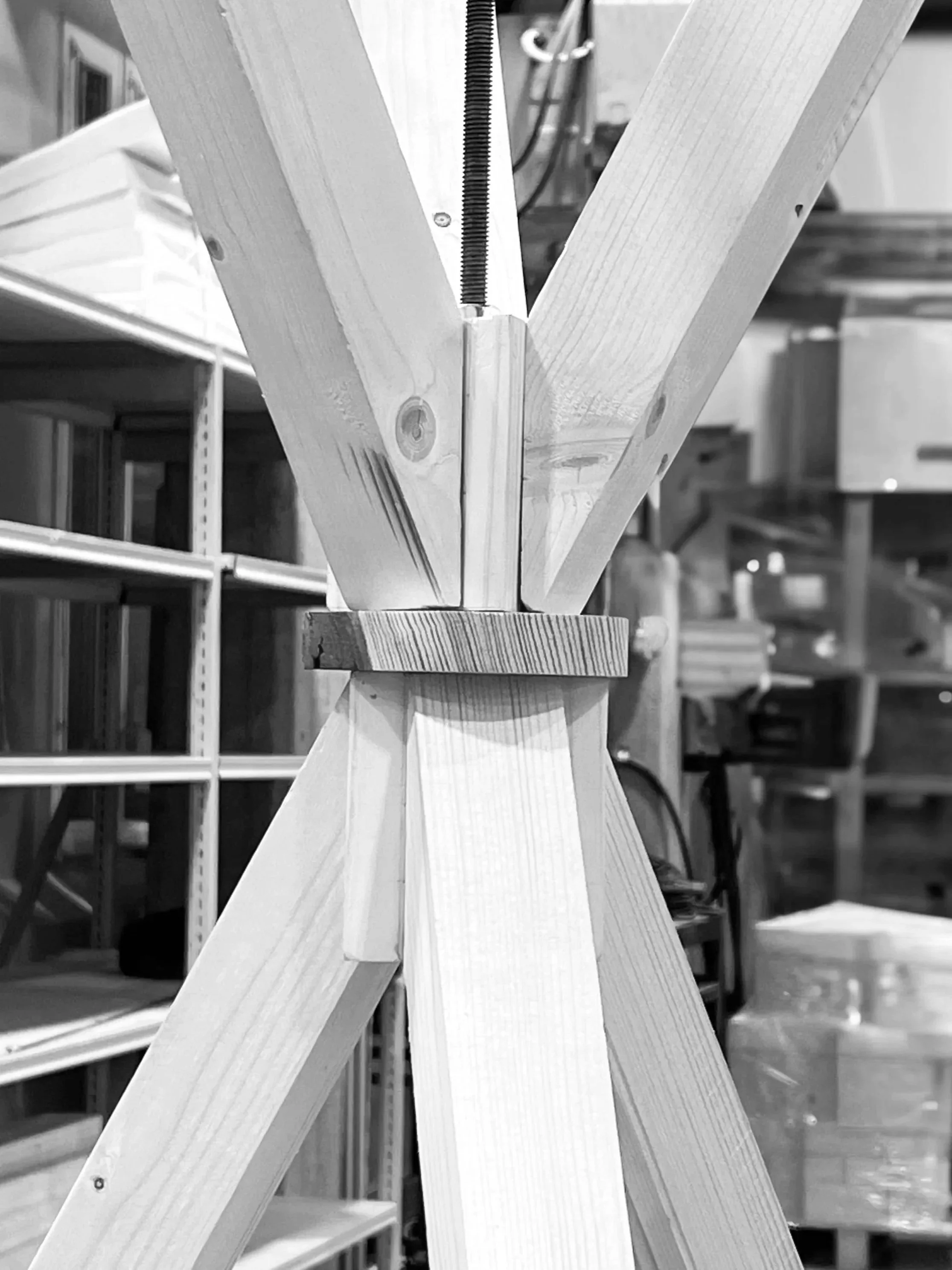 Close-up of a wooden tripod with a central joint, set up in a workshop with shelves and tools in the background.
