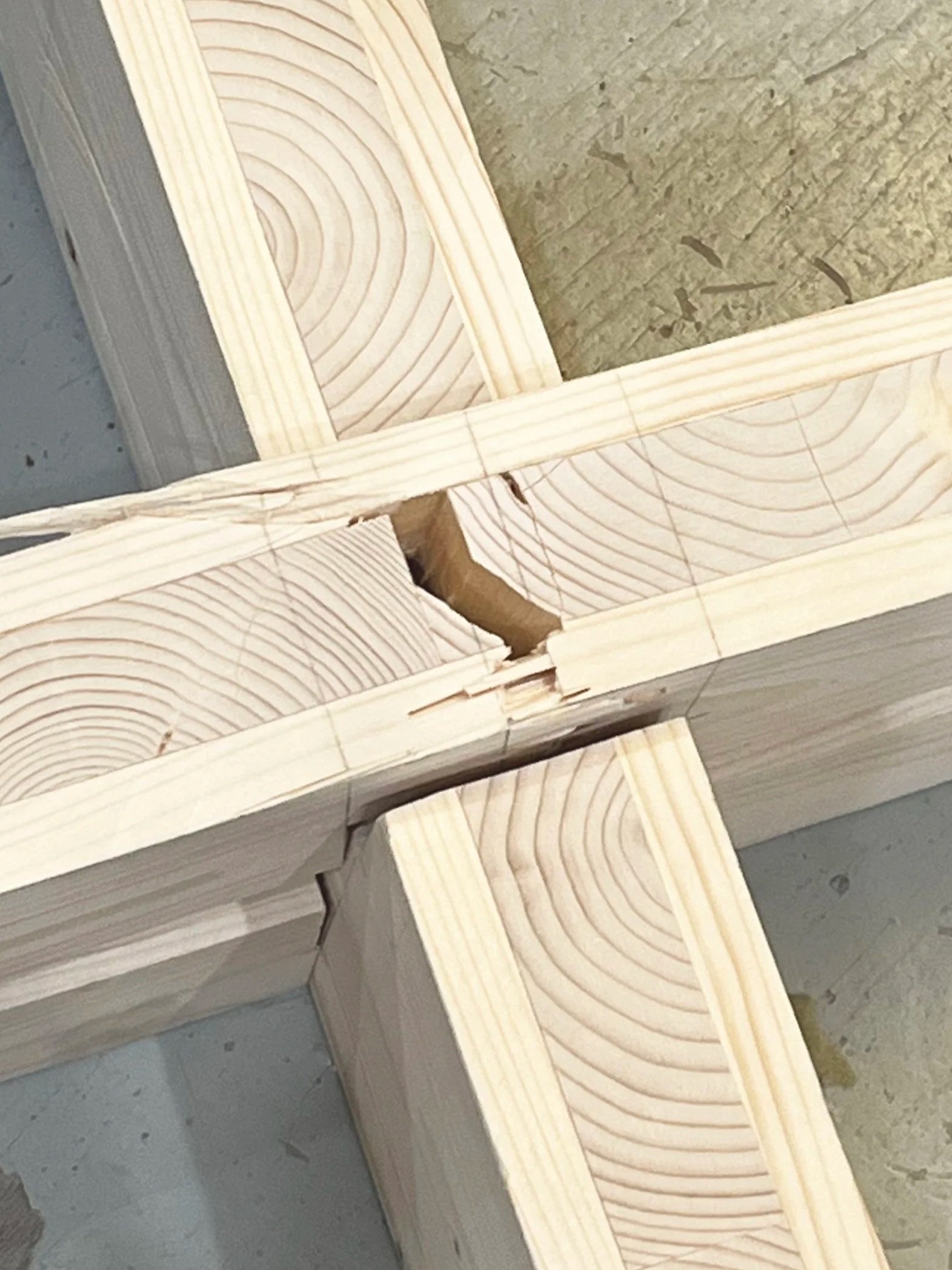 A close-up view of assembled wooden beams with visible wood grain and cross marks, on a workshop floor.