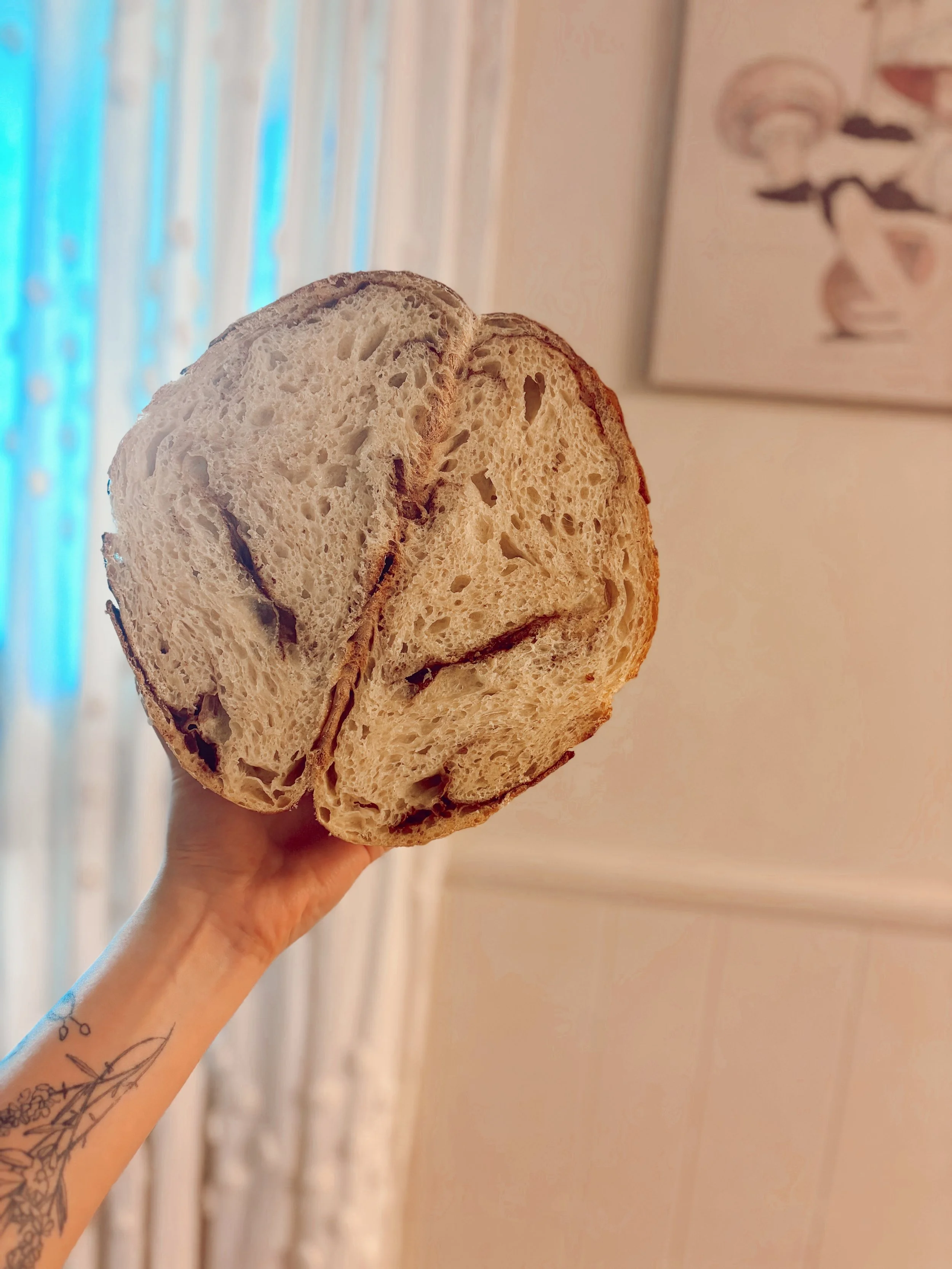Person holding a loaf of sliced sourdough bread with a visible tattoo on their arm in a warmly lit room.